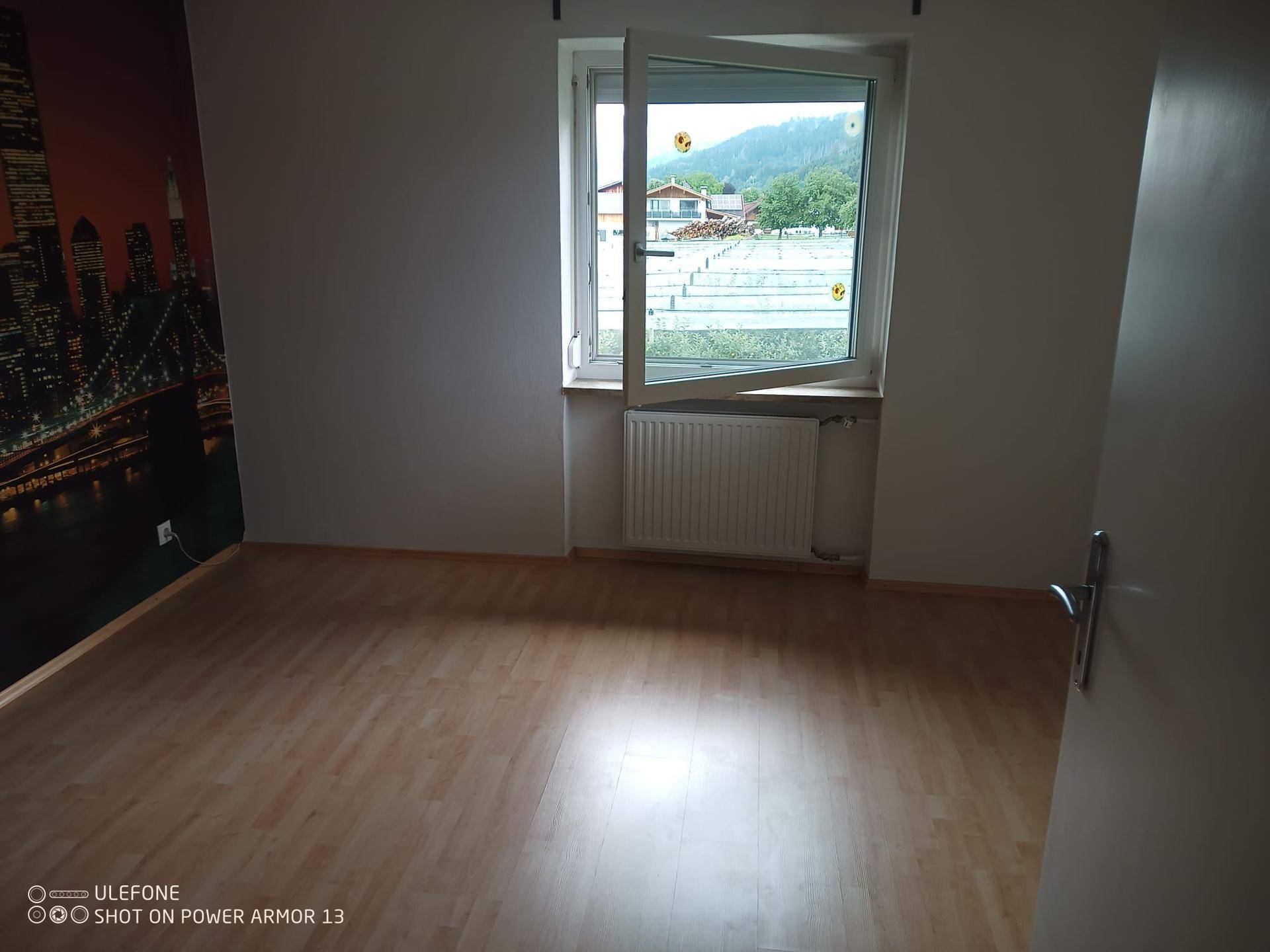 Schlafzimmer mit Laminatboden, Fenster und Blick auf die grüne Landschaft.