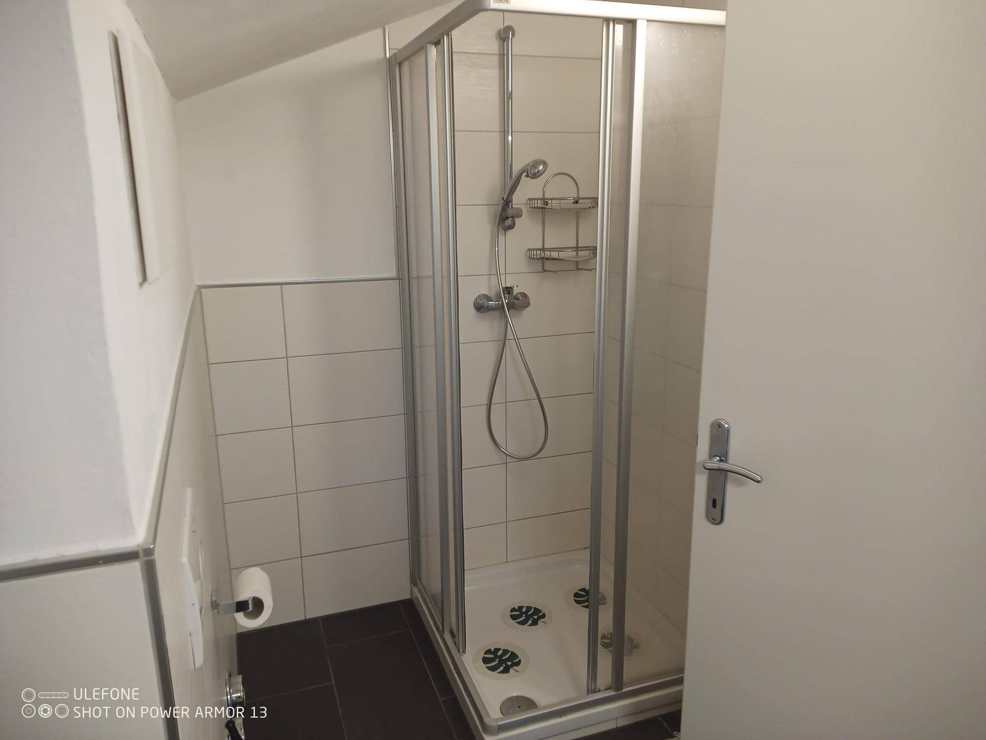 Badezimmer mit Duschkabine, weißen Fliesen und dunklem Boden.
