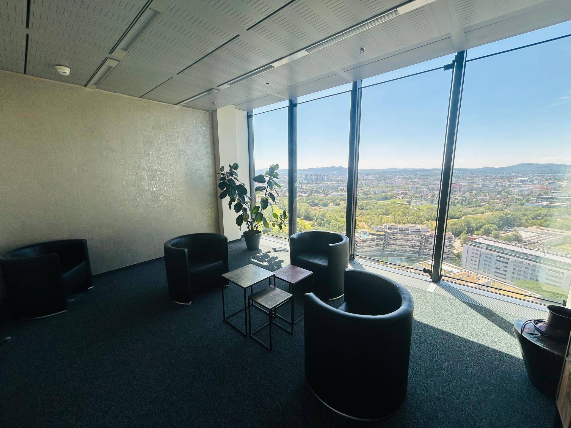 Heller Bürobereich mit bequemen Sesseln, großen Fenstern und weitem Blick über die Stadt und Landschaft.