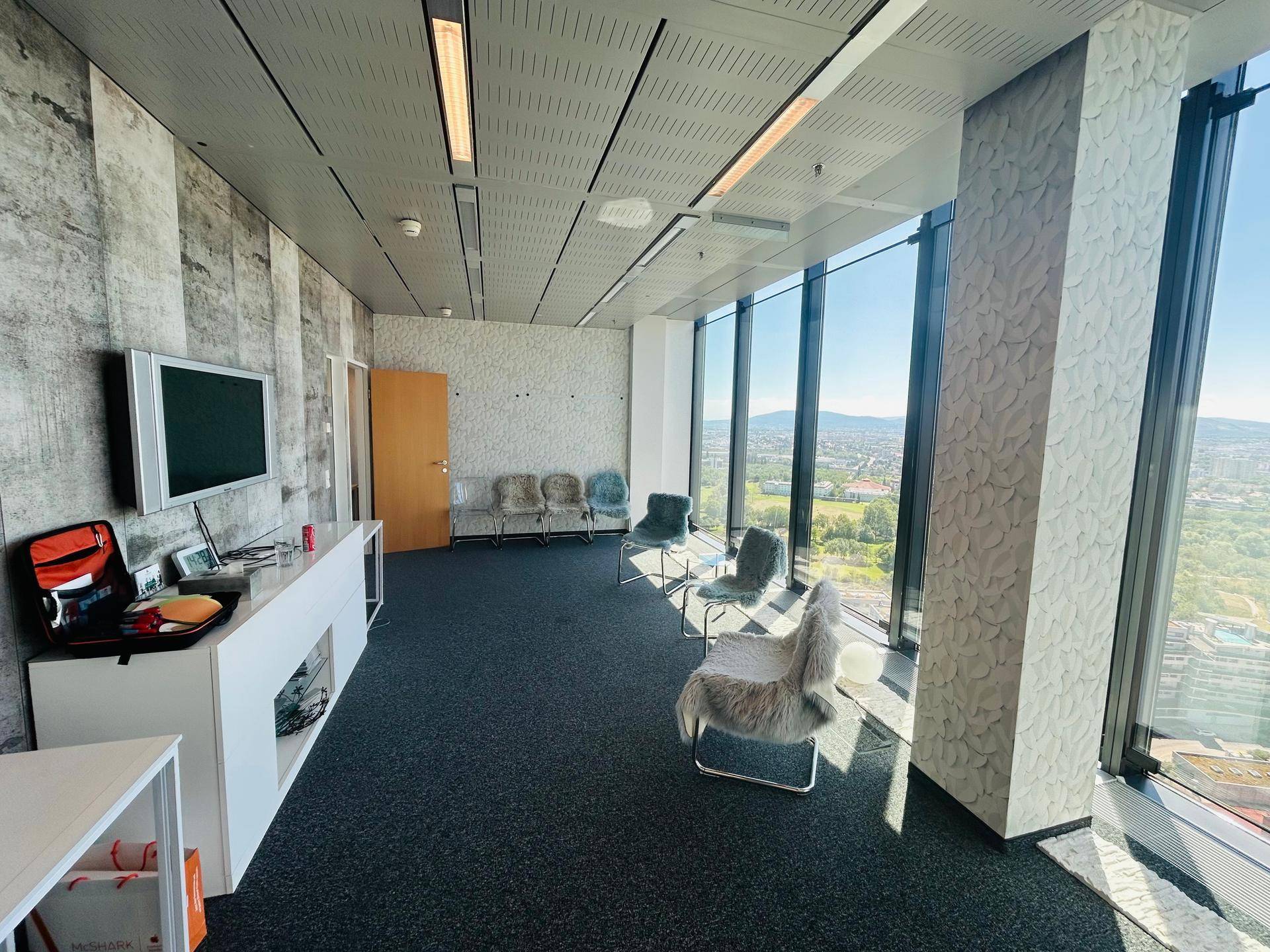 Moderner Bürobereich mit TV-Wand, bequemen Sitzgelegenheiten und weitreichendem Blick über die Umgebung.
