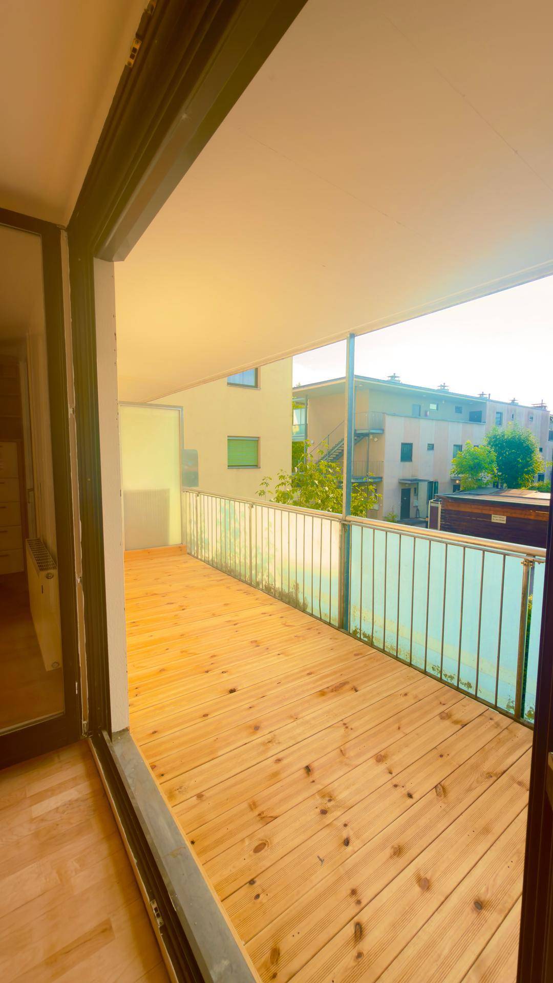 Geräumiger Balkon mit Holzbelag und Blick auf die umliegenden Gebäude und Grünflächen.