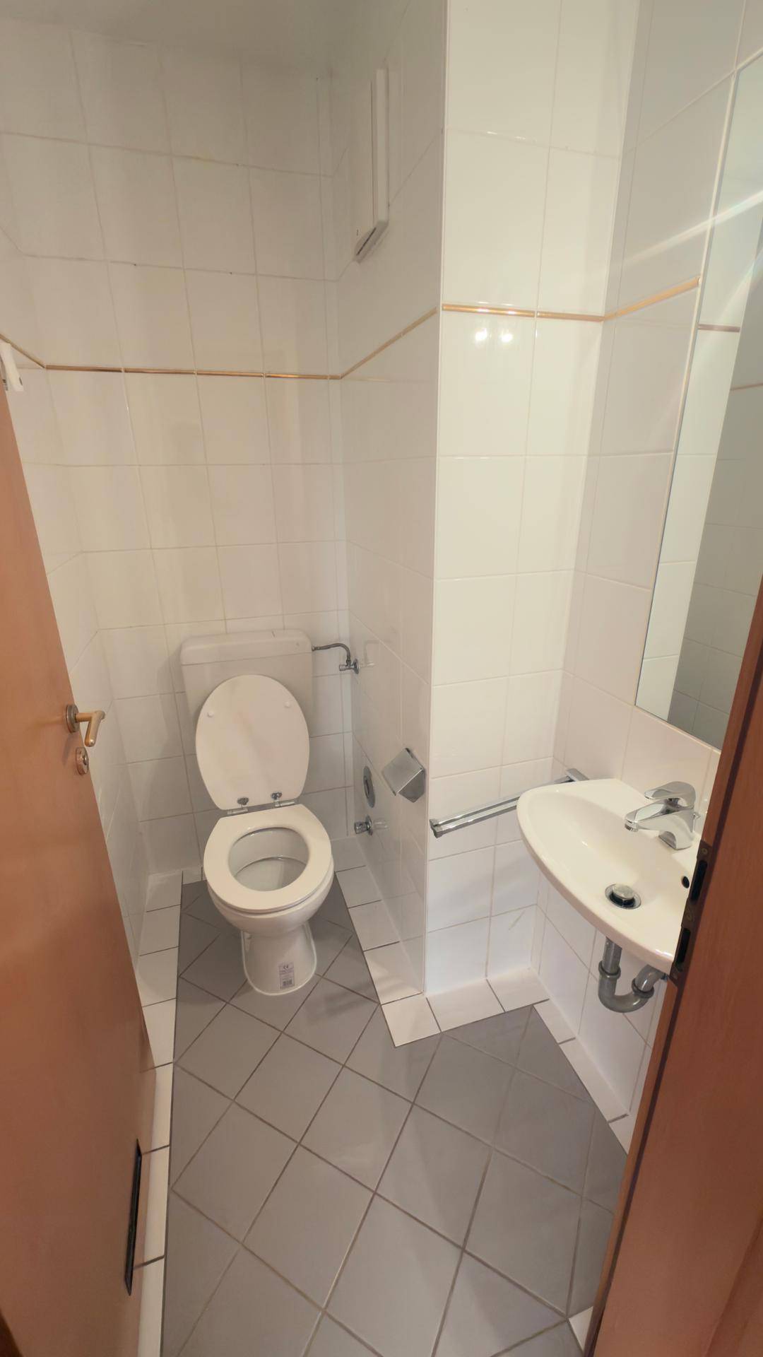 Kleines Gäste-WC mit weißen Fliesen, Toilette und Waschbecken, funktional eingerichtet.