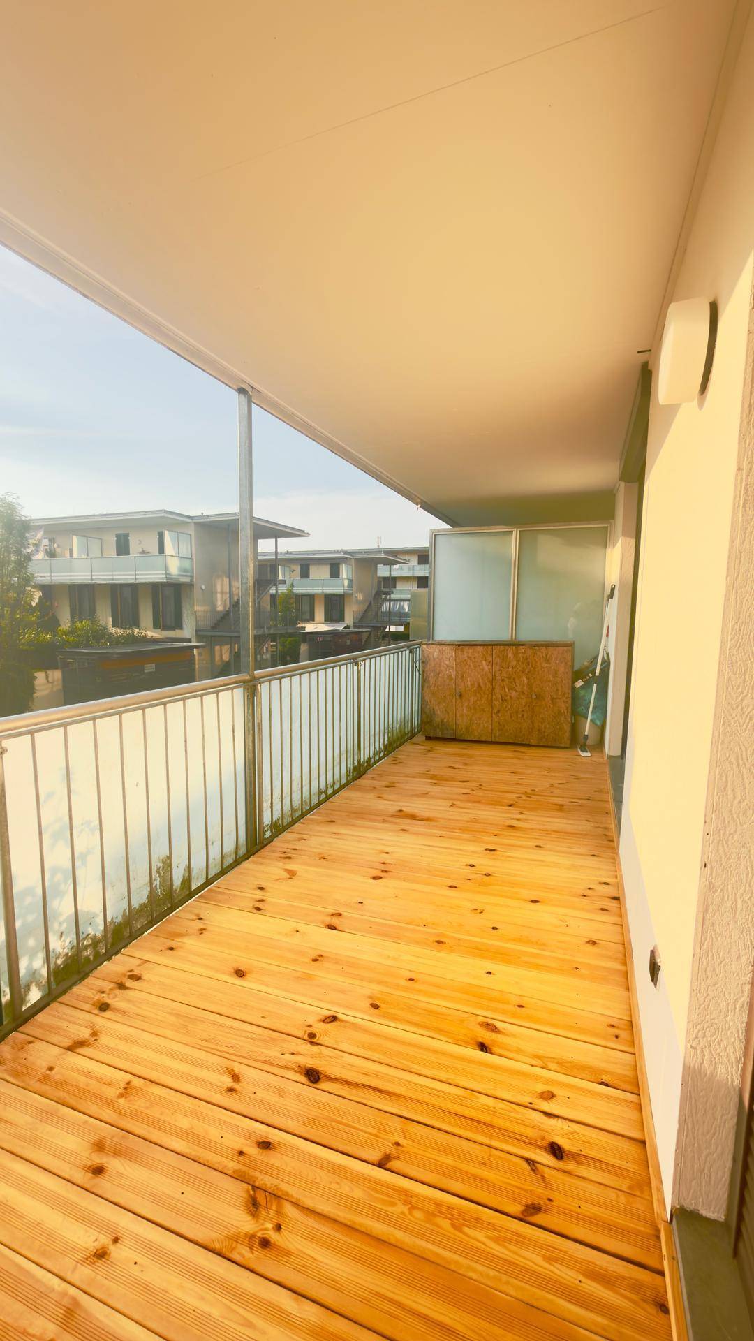 Langer Balkon mit Holzbelag und Glasgeländer, der einen Blick auf die Umgebung bietet.