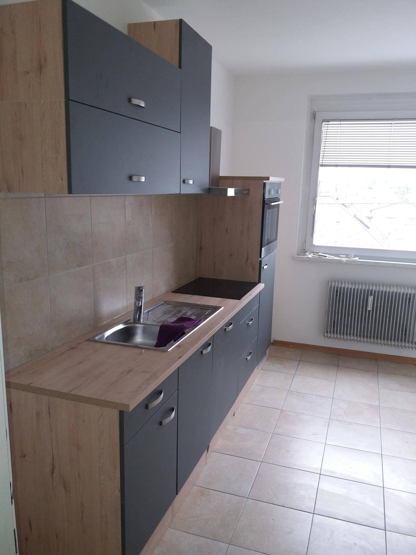 Moderne Küche mit grauen und holzfarbenen Schränken, Induktionskochfeld und Backofen.