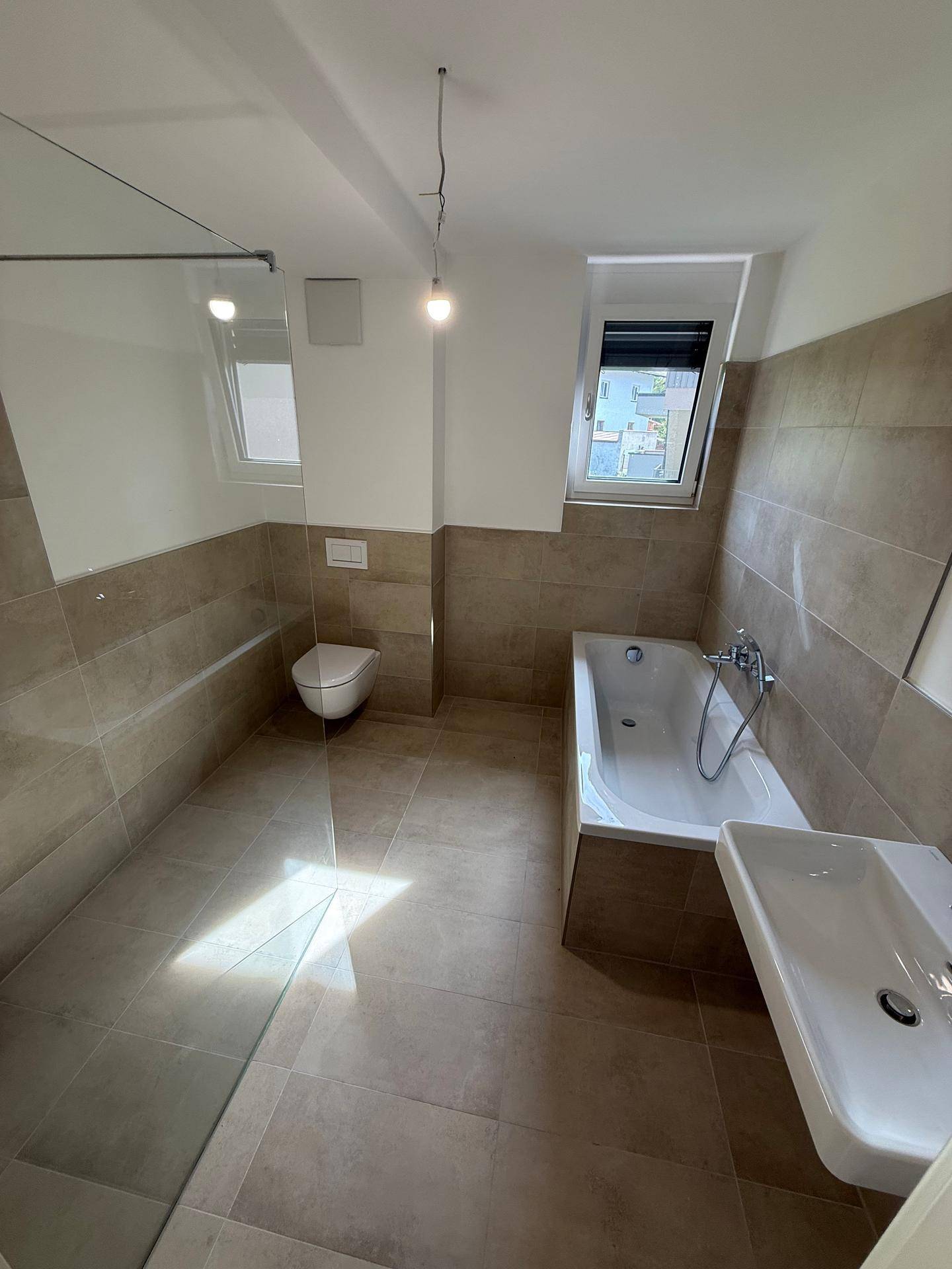 Modernes Badezimmer mit Badewanne, Dusche, WC und großformatigen Fliesen.