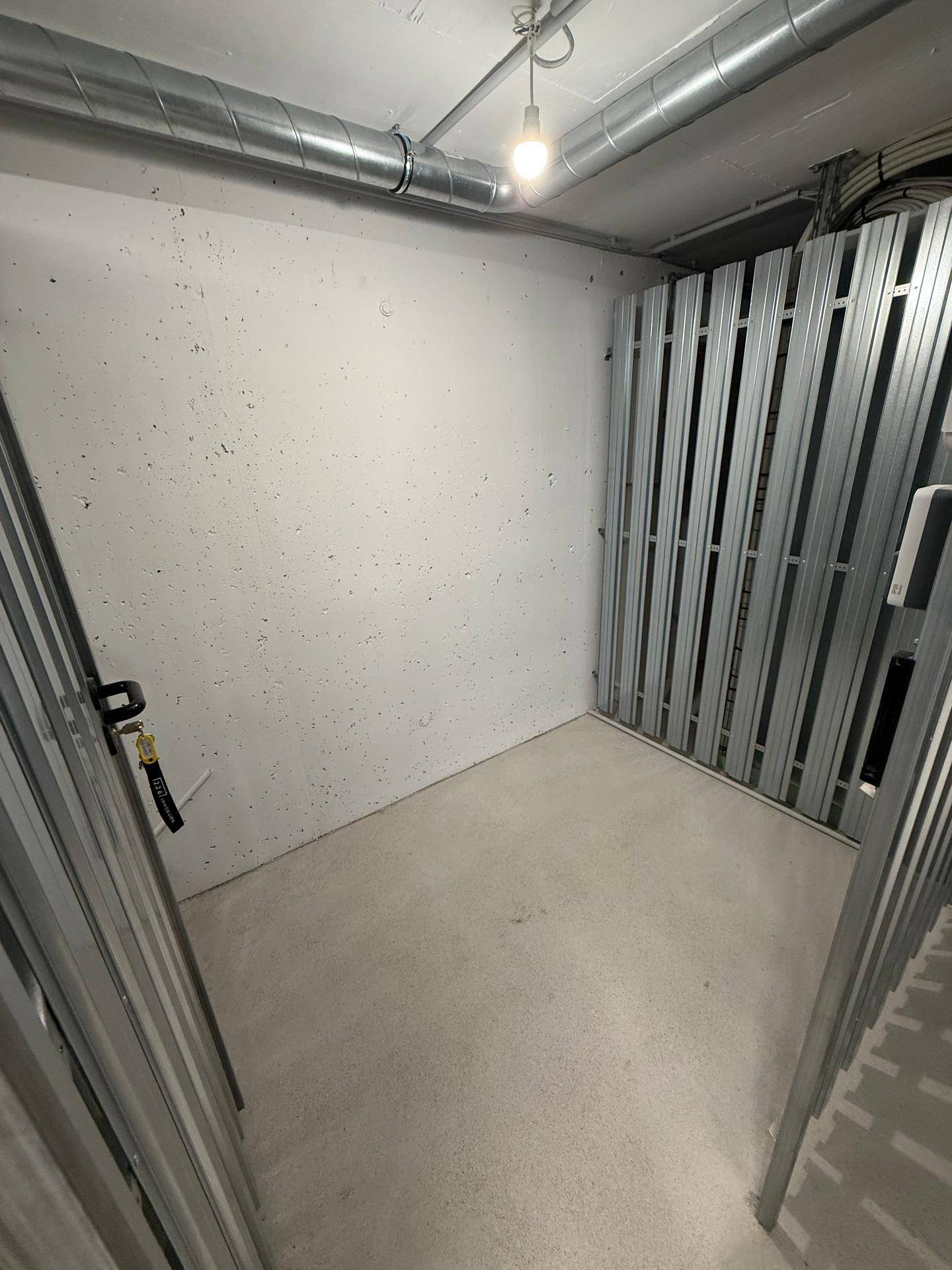 Praktischer Abstellraum im Keller mit Betonboden und Metallabtrennungen.