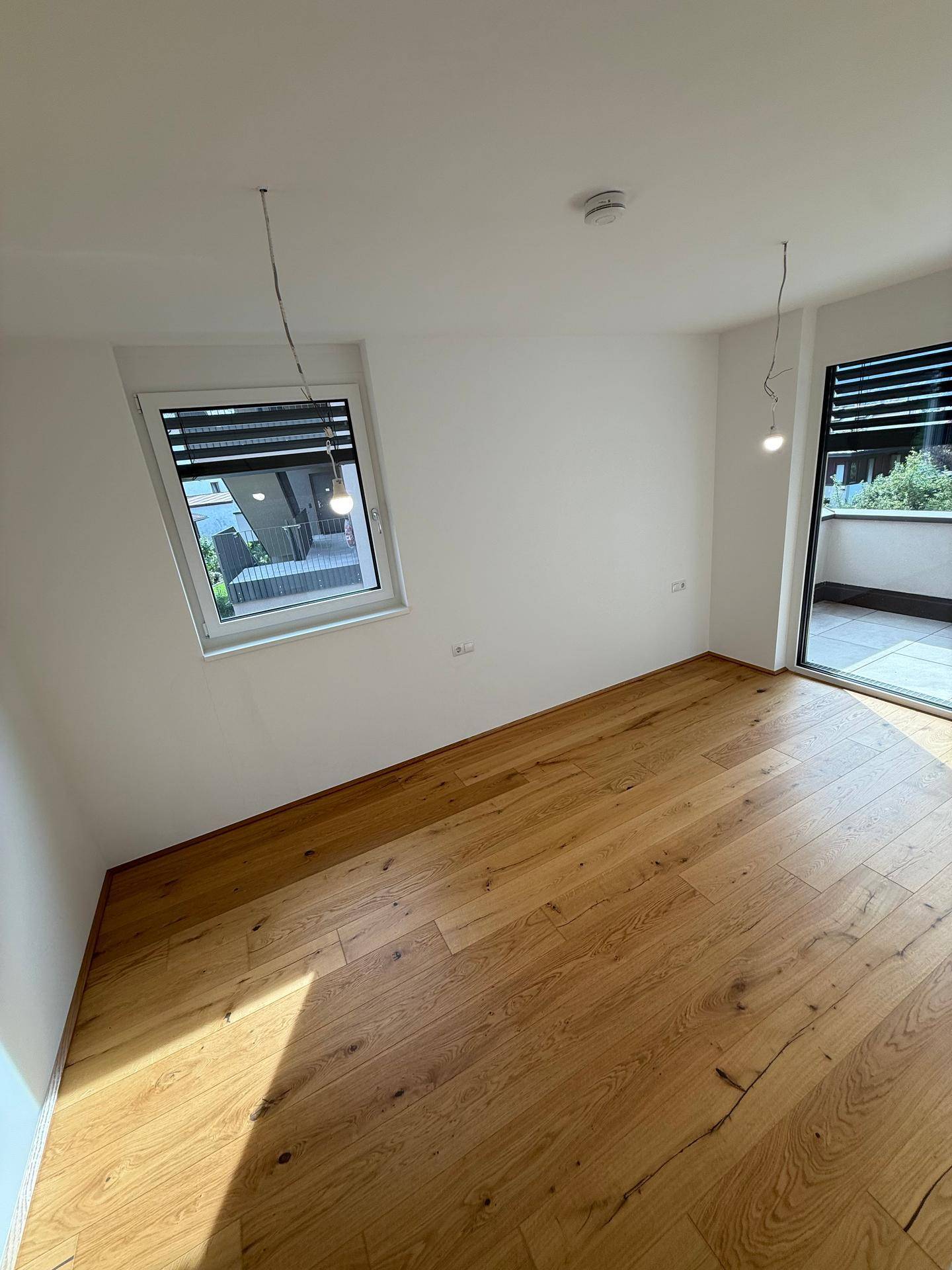 Geräumiges Schlafzimmer mit Holzboden, viel Licht und Zugang zum Balkon.