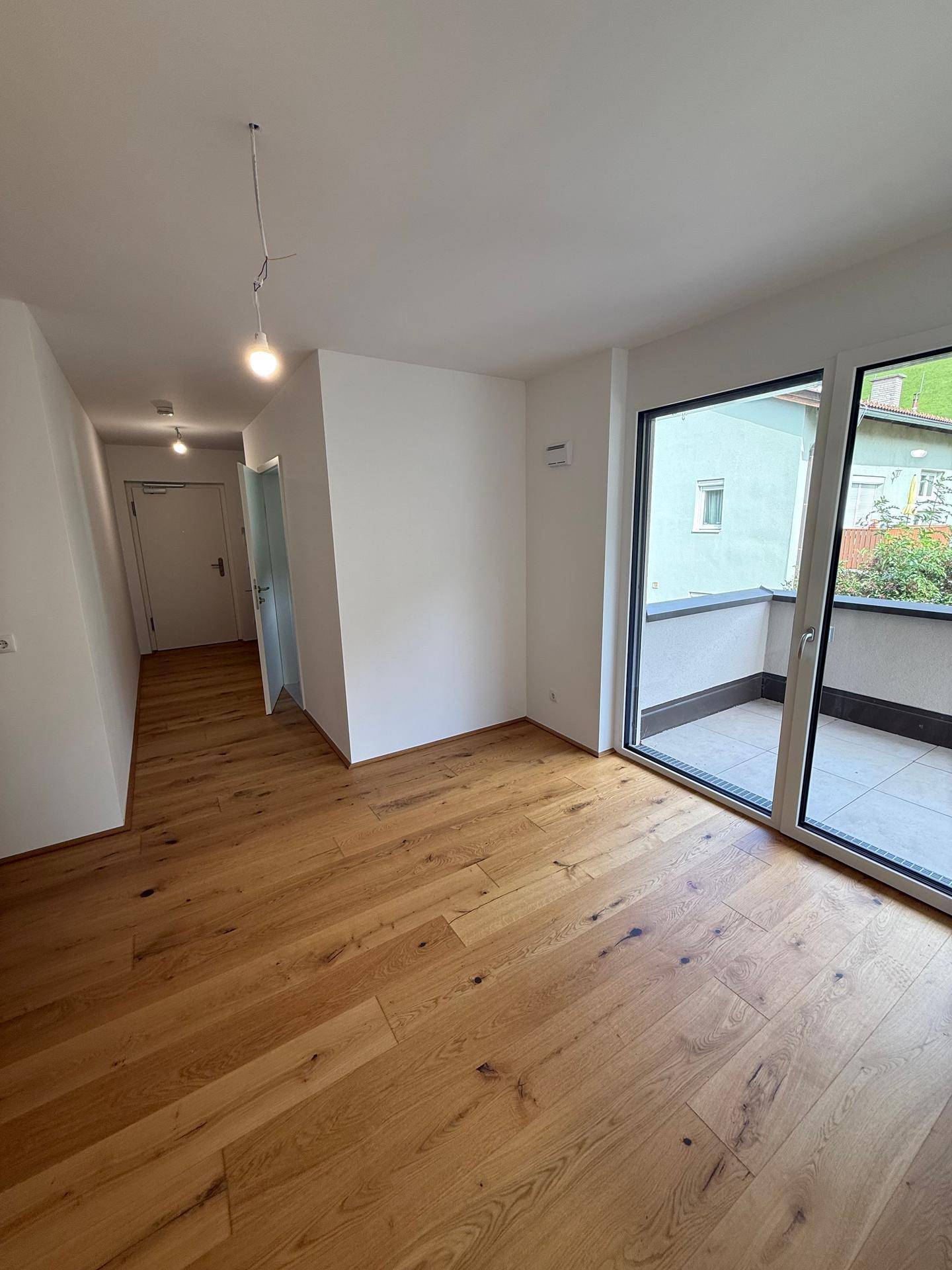 Geräumiger Wohnbereich mit Holzboden, viel Tageslicht und Zugang zum Balkon.