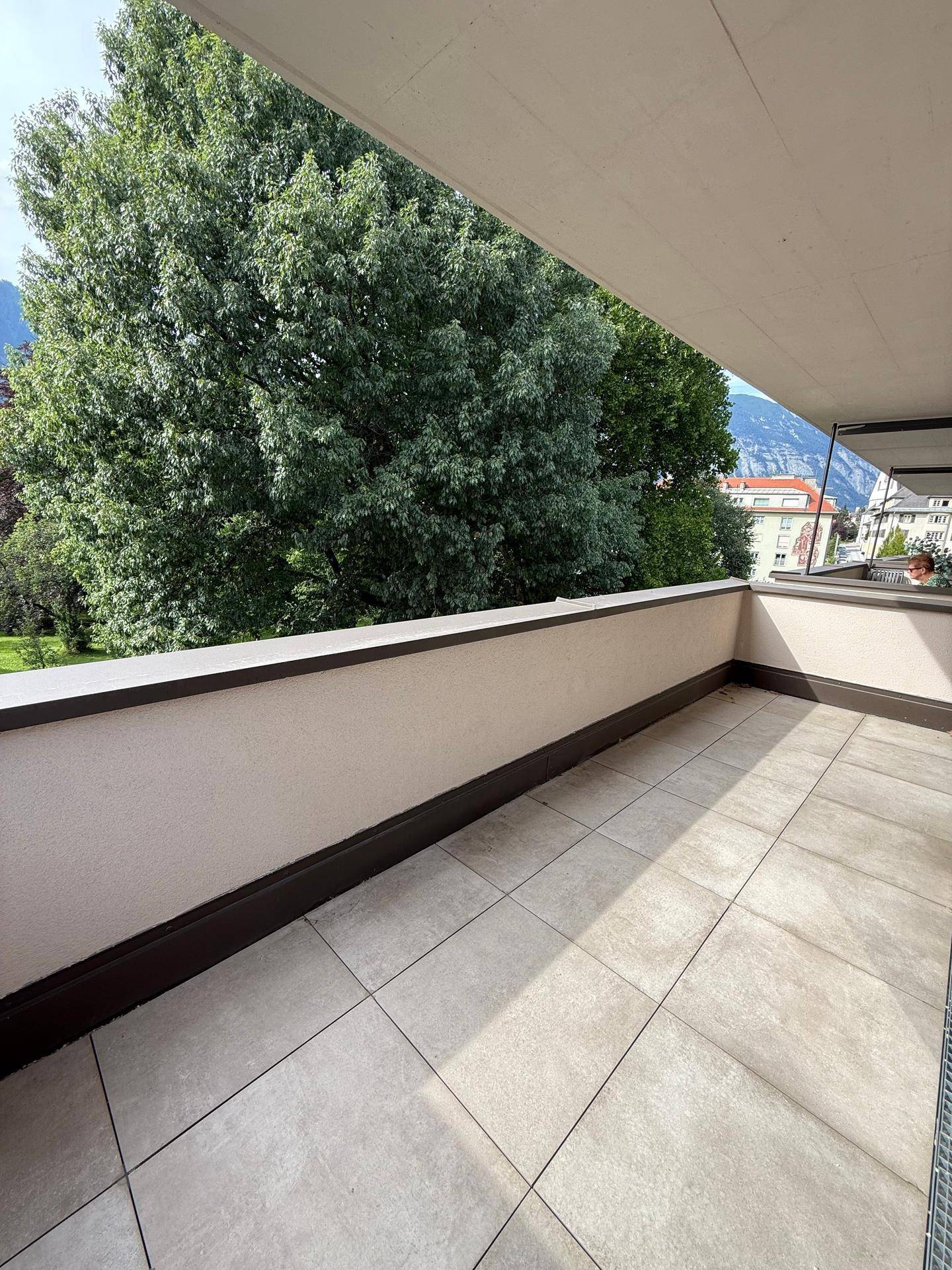 Geräumiger Balkon mit Fliesenboden und Blick auf grüne Bäume und die Umgebung.