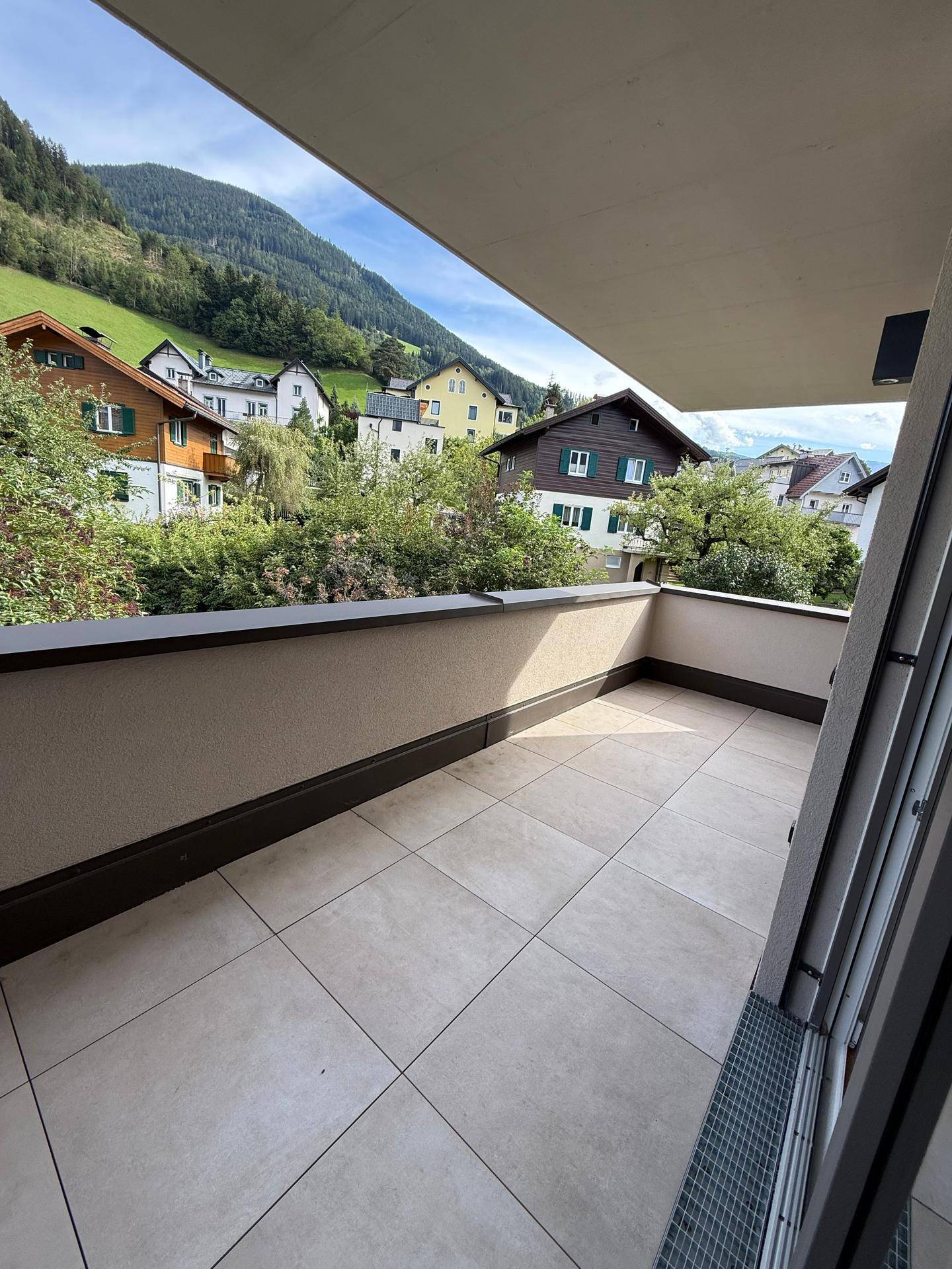 Sonniger Balkon mit Fliesenboden und Blick auf die umliegende Berglandschaft.