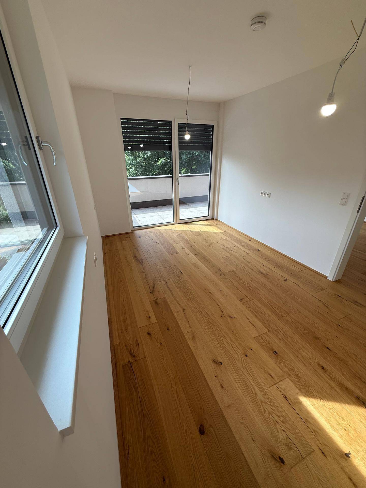Helles Schlafzimmer mit Holzboden und großen Fenstern, die viel Tageslicht hereinlassen.