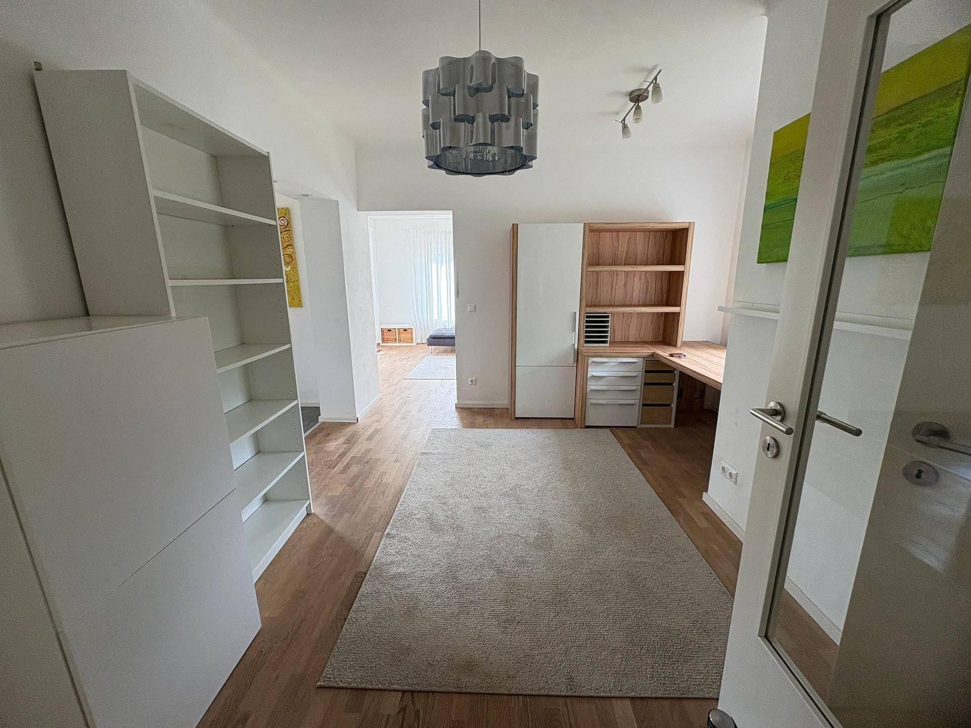 Heller Flur oder offener Bereich mit Holzboden, weißen Regalen und einem Arbeitsbereich im Hintergrund.