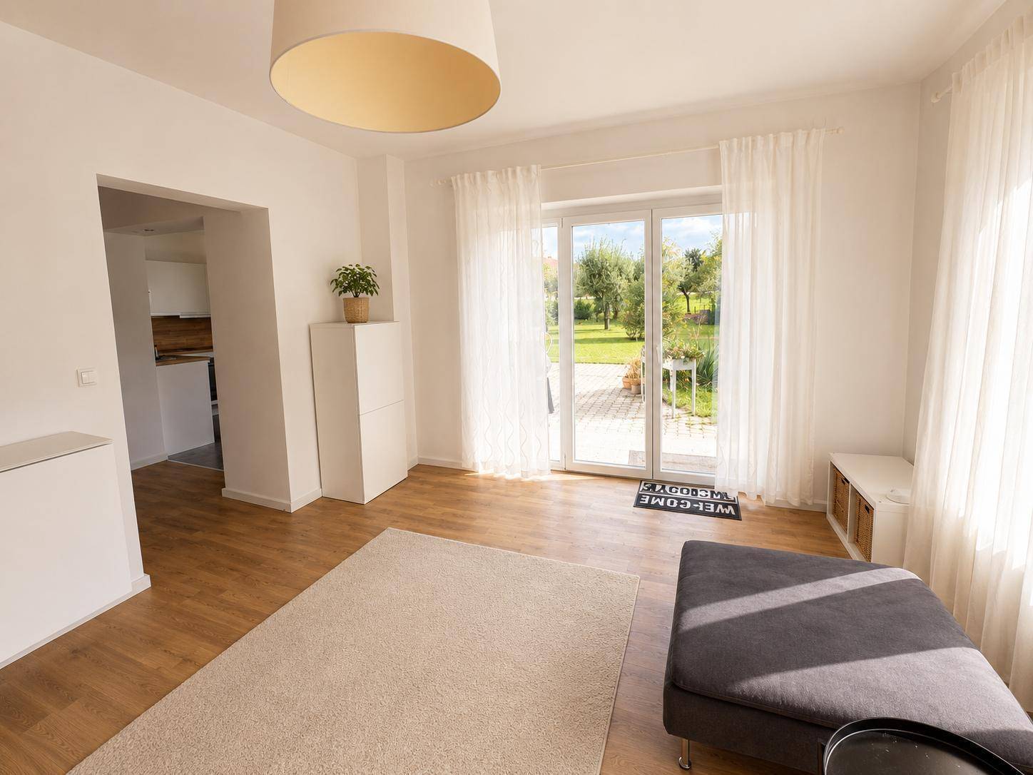Helles Wohnzimmer mit Zugang zur Terrasse und Blick in den Garten, ausgestattet mit Holzboden und hellen Wänden.