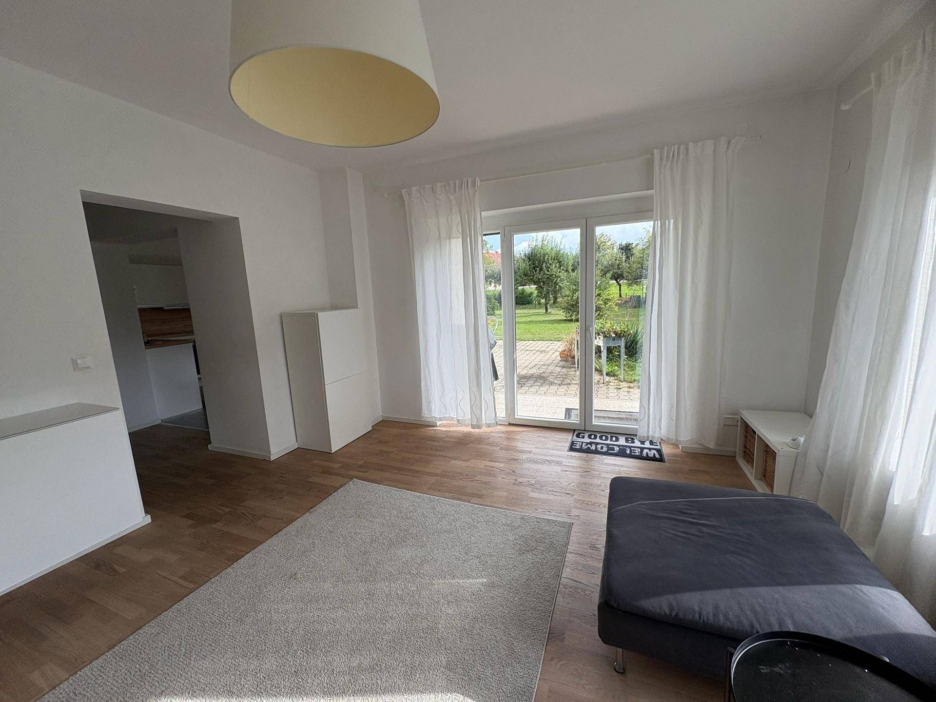 Wohnzimmer mit Zugang zur Terrasse und Blick in den Garten, ausgestattet mit Holzboden und hellen Wänden.