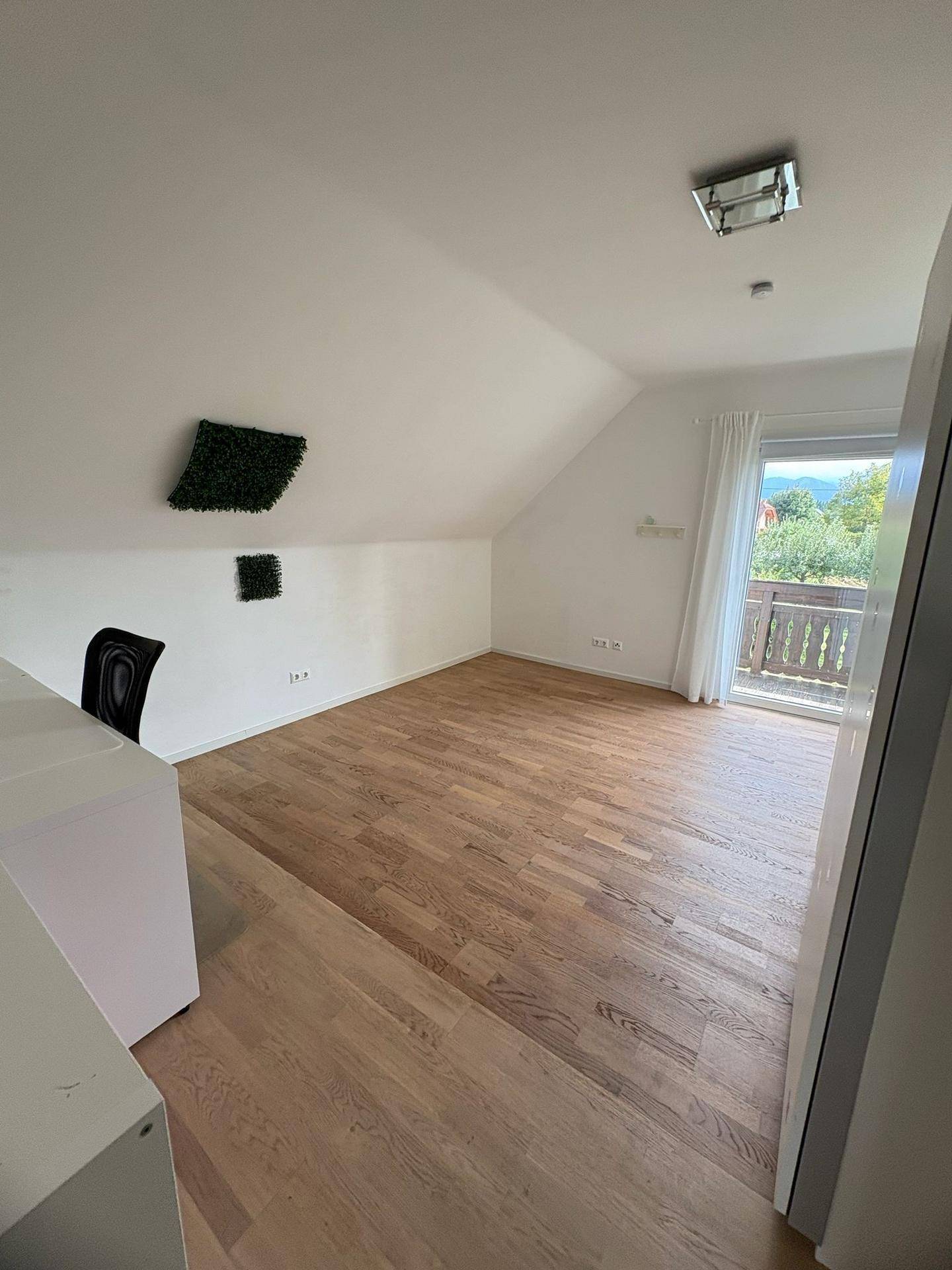 Geräumiges Schlafzimmer im Dachgeschoss mit Holzboden und einem Fenster mit Blick auf die Umgebung.