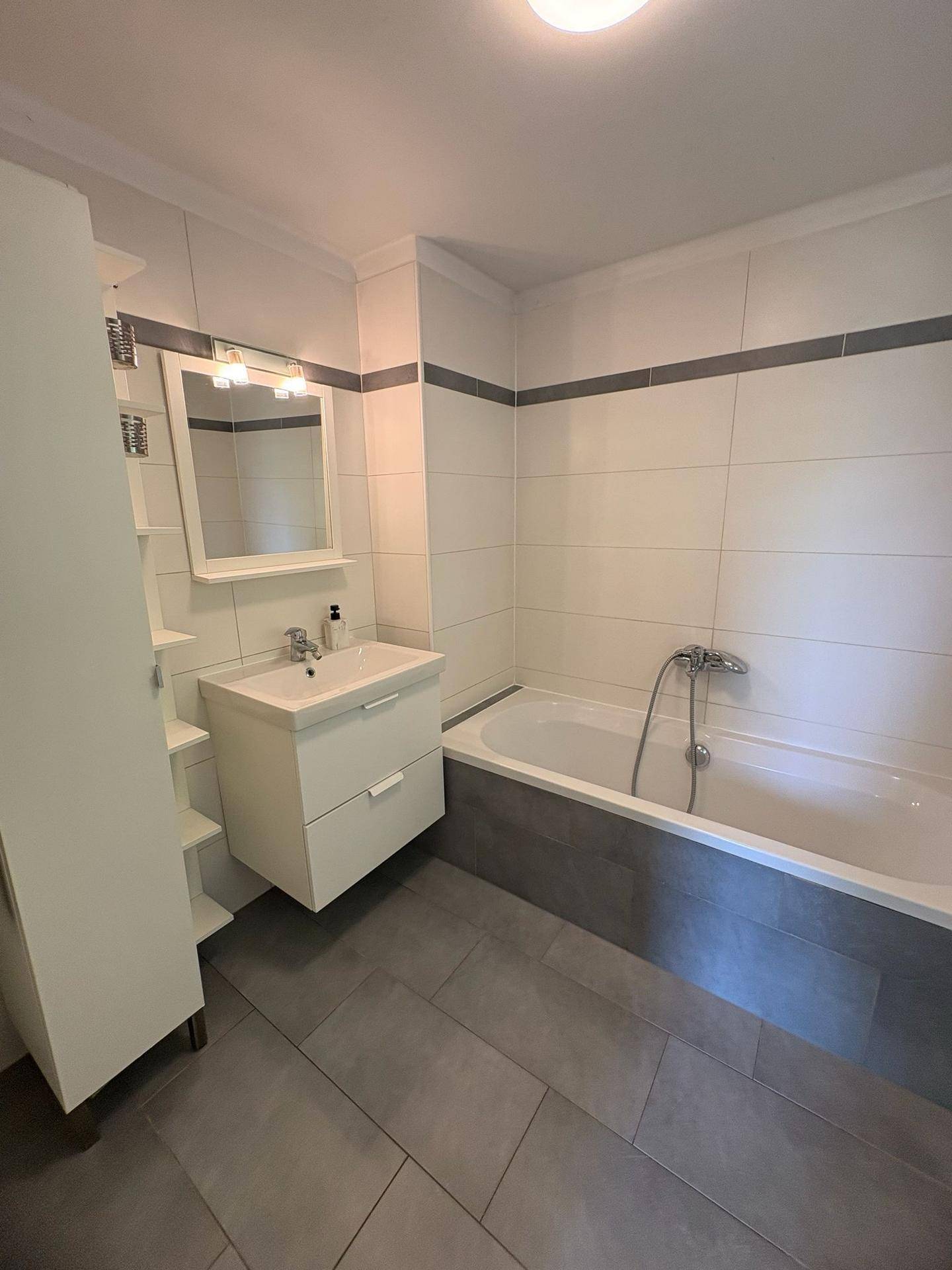 Badezimmer mit Badewanne, modernem Waschtisch und grauen Fliesen am Boden und an den Wänden.