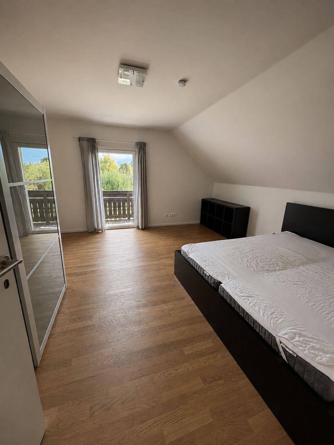 Schlafzimmer im Dachgeschoss mit Holzboden, Zugang zum Balkon und Blick ins Grüne.