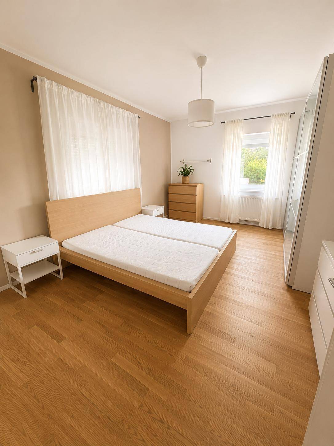 Schlafzimmer mit Doppelbett, Holzboden und einem Fenster, das viel natürliches Licht hereinlässt.