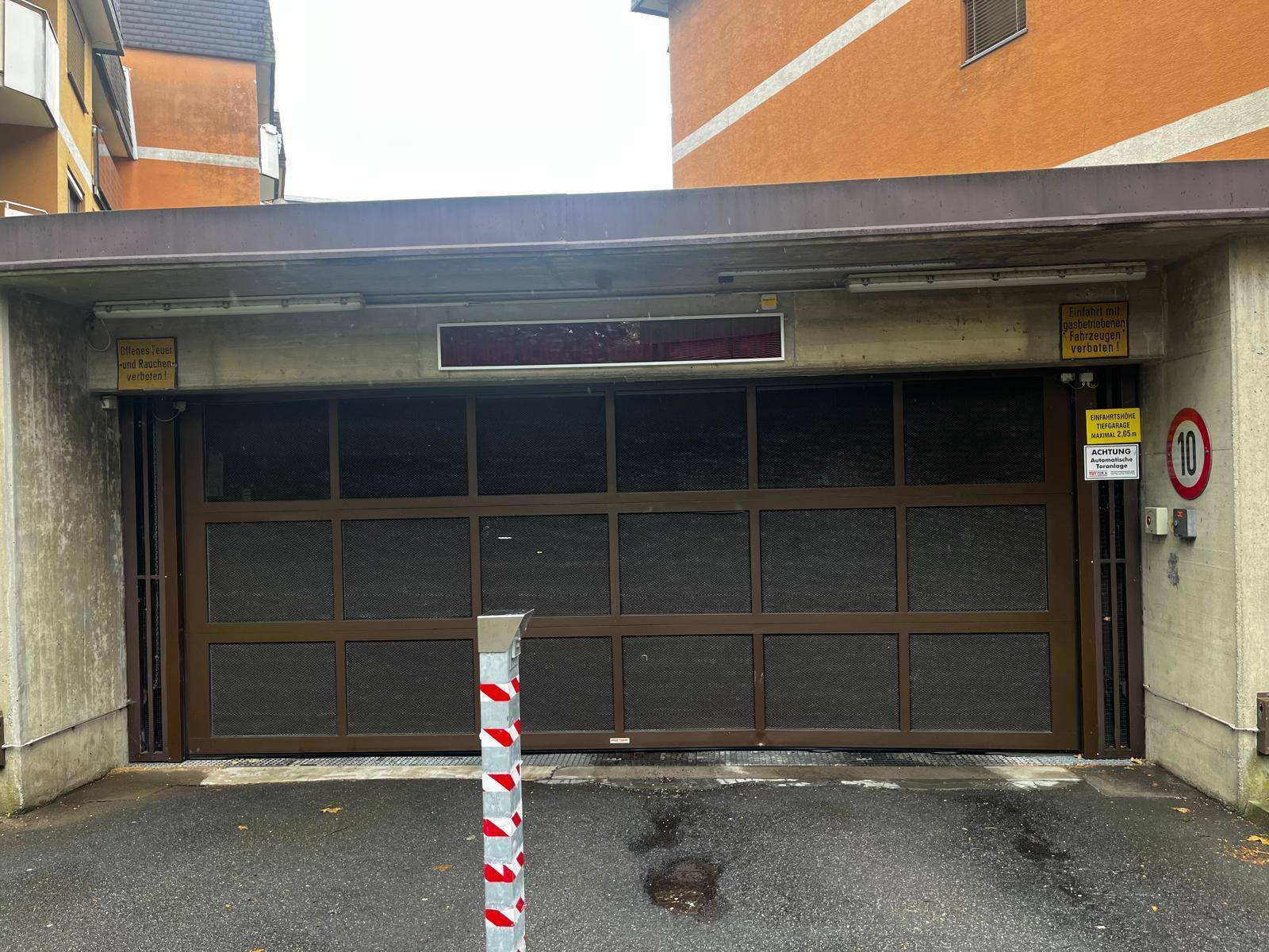 Einfahrt zur Tiefgarage mit einem braunen Garagentor und der Betonfassade des Gebäudes.