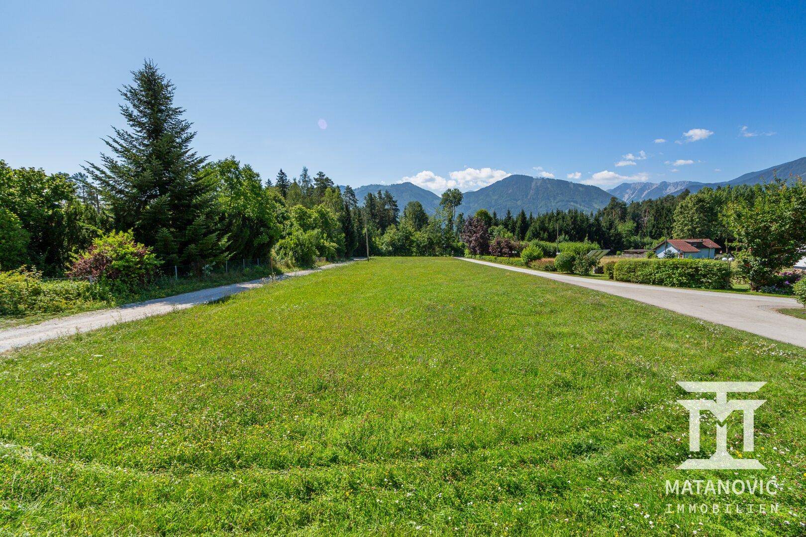 Weitläufiges, sonniges Wiesengrundstück mit Blick auf die umliegende Berglandschaft und klare Wege.