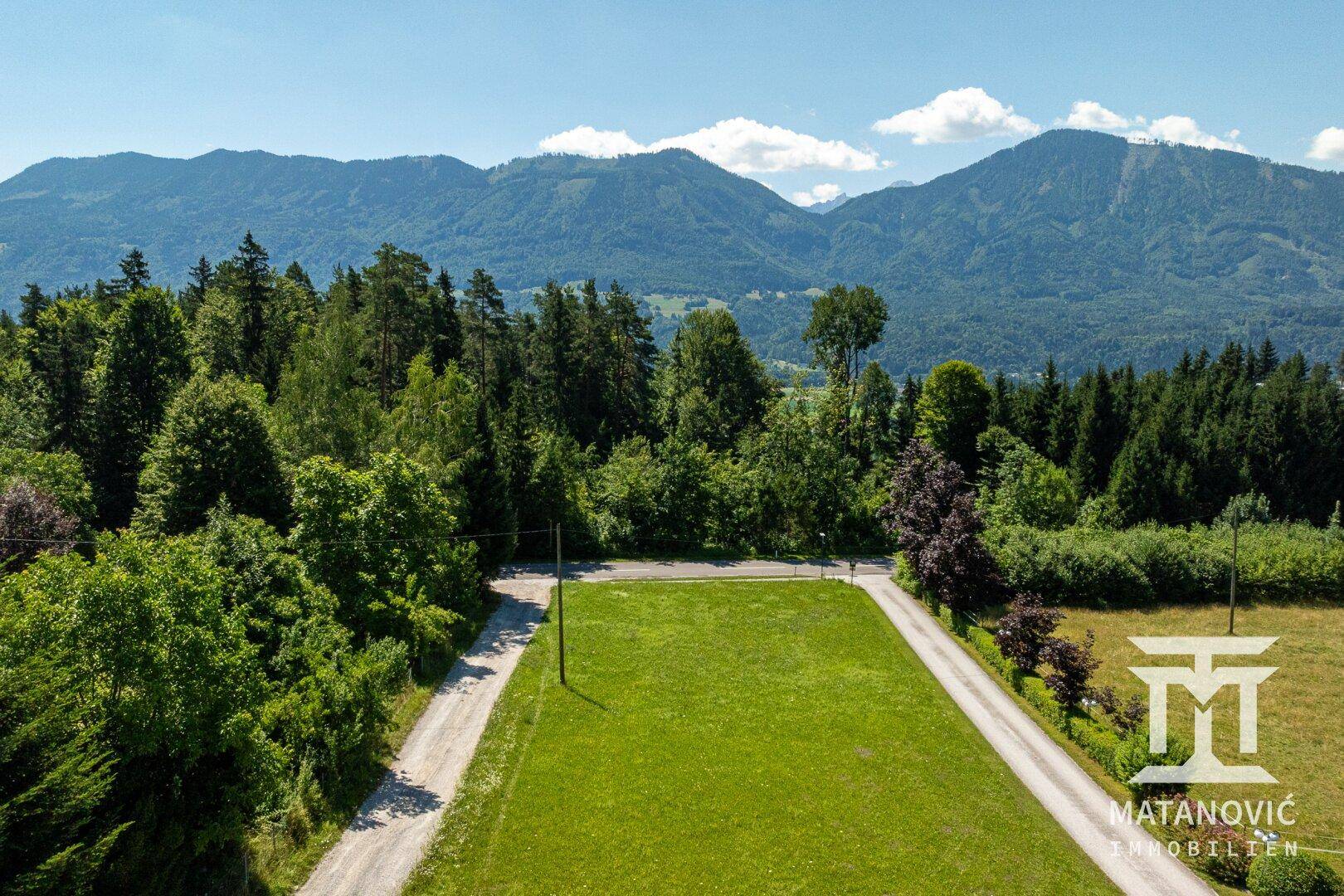 Luftaufnahme eines weitläufigen grünen Grundstücks, umgeben von Wald und Zufahrtswegen.