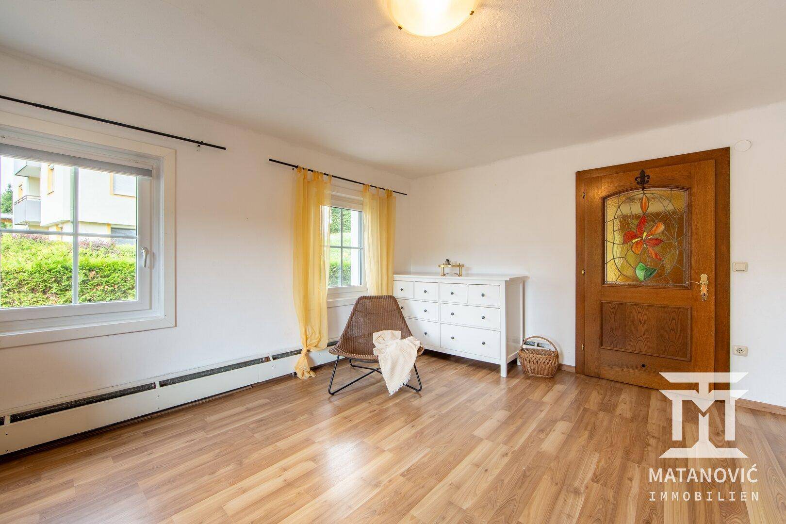 Heller Raum mit Laminatboden, weißen Wänden und einer Holztür mit Buntglasfenster.