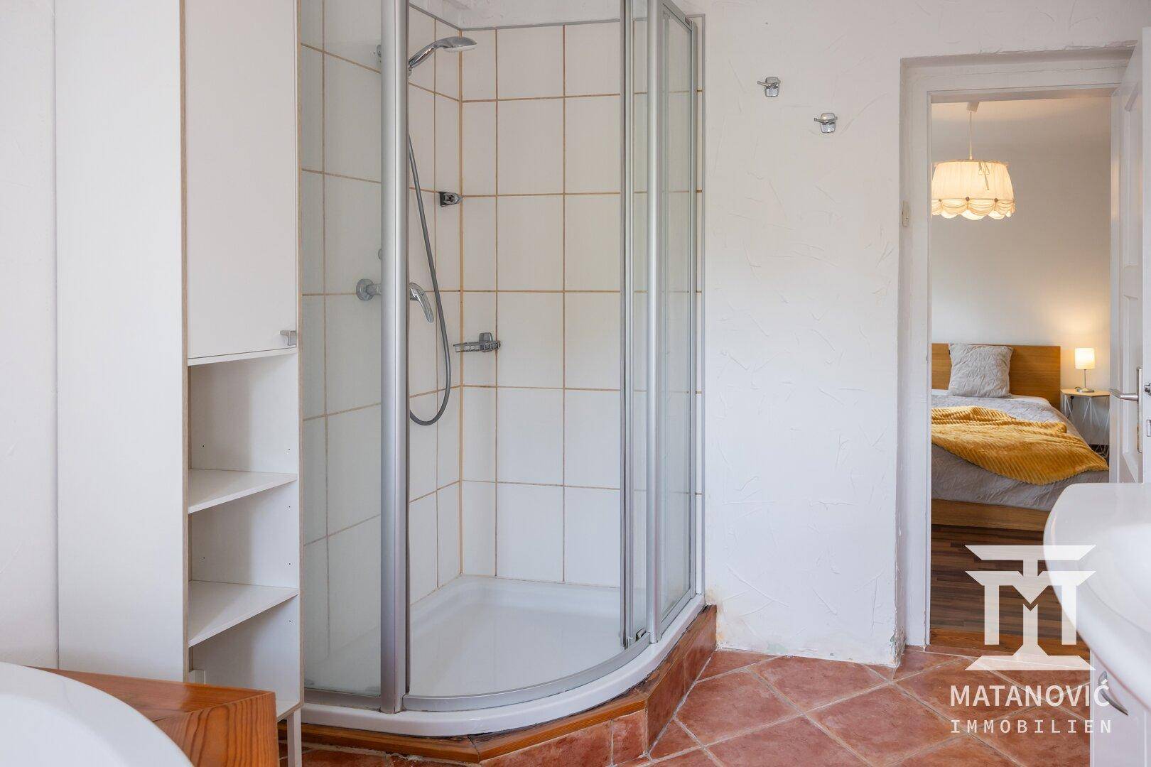 Badezimmer mit Duschkabine, Terrakottafliesen und Zugang zum angrenzenden Schlafzimmer.