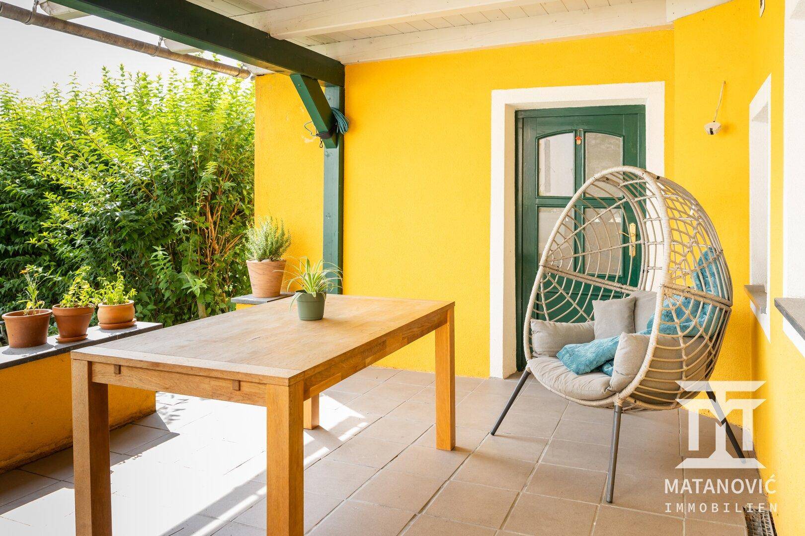 Überdachte Terrasse mit Holztisch und Hängesessel, ideal für entspannte Stunden im Freien.