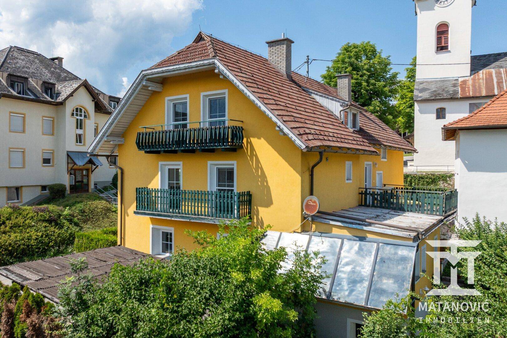 Rückansicht des gelben Hauses mit mehreren Balkonen und einem Anbau mit Flachdach.