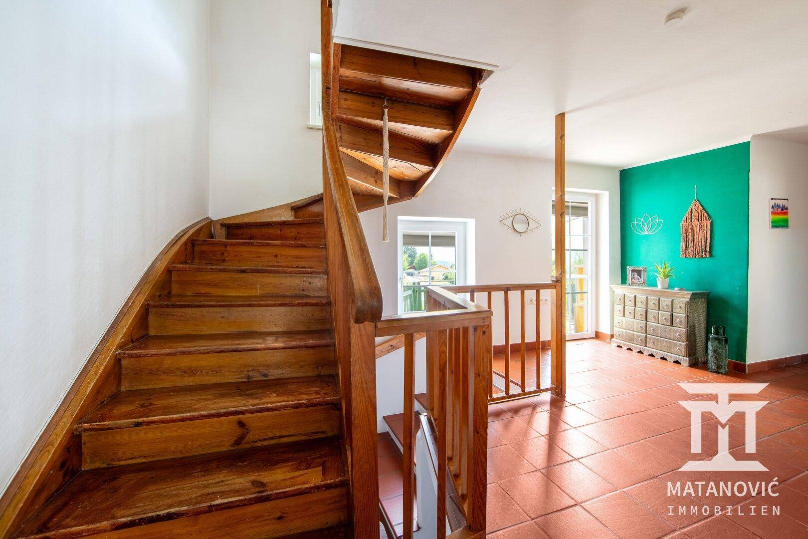 Holztreppe führt in die obere Etage, mit Terrakottafliesen und einer grünen Akzentwand.