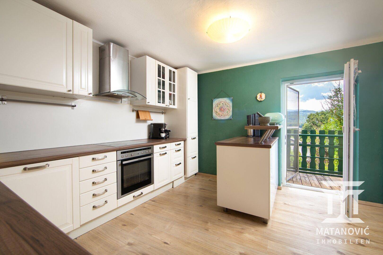 Moderne Küche mit weißen Schränken, Holz-Arbeitsplatten und Zugang zu einem Balkon.