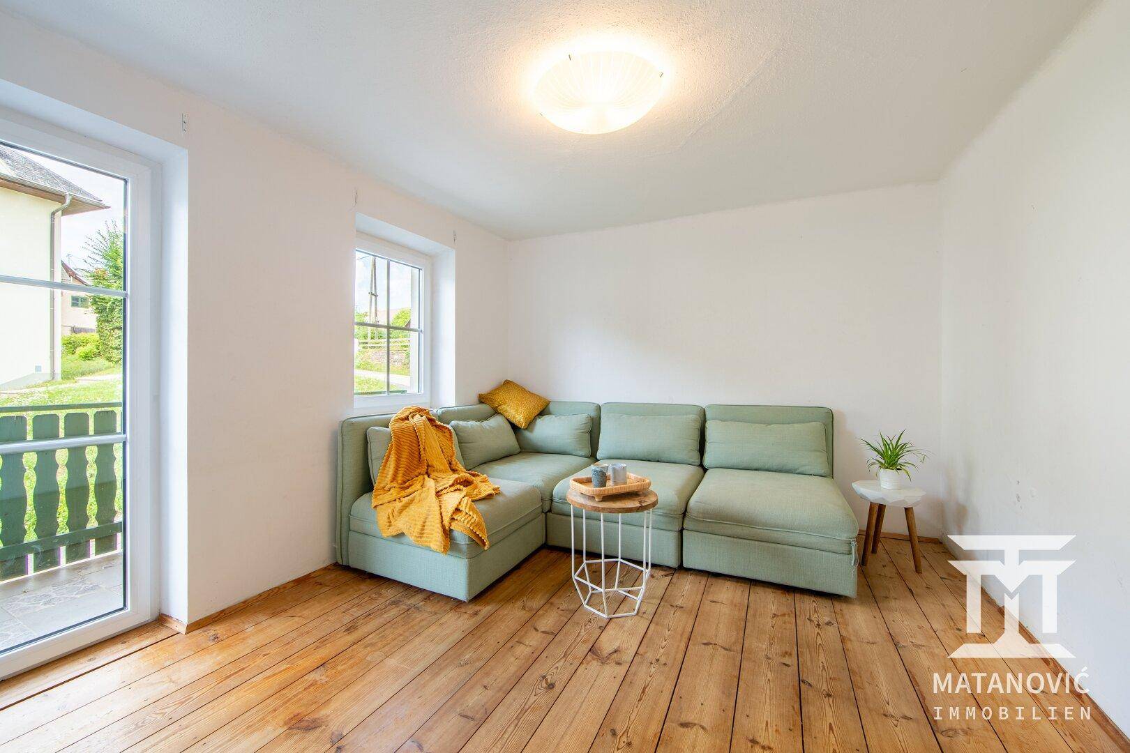 Helles Wohnzimmer mit hellgrünem Ecksofa, Dielenboden und Zugang zu einem Balkon.