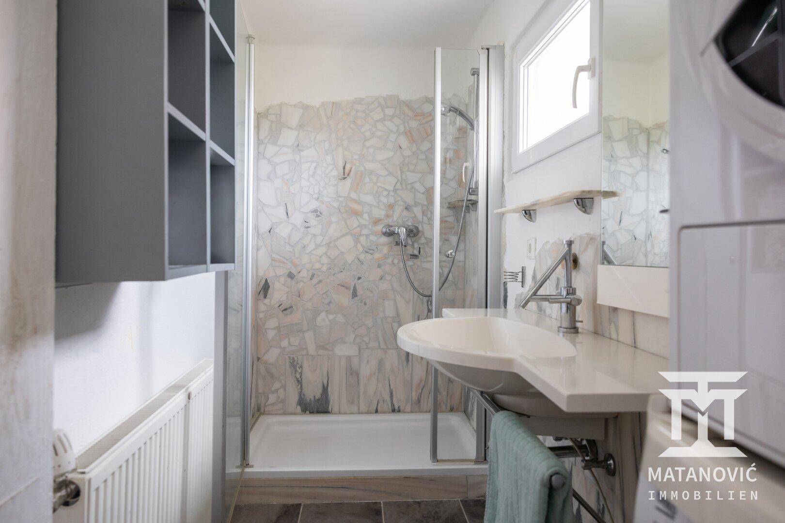 Modernes Badezimmer mit Duschkabine, Einzelwaschbecken und Fenster, sowie Mosaikfliesen.