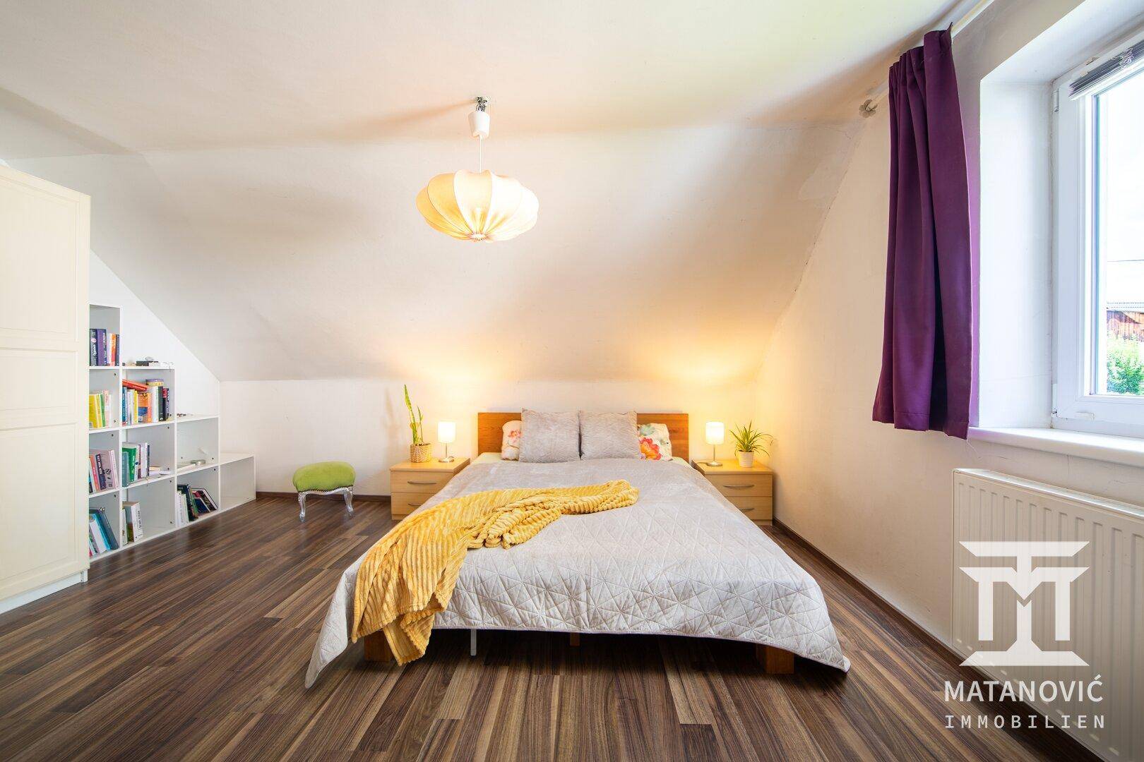 Gemütliches Schlafzimmer im Dachgeschoss mit schrägen Wänden, dunklem Laminatboden und Fenster.