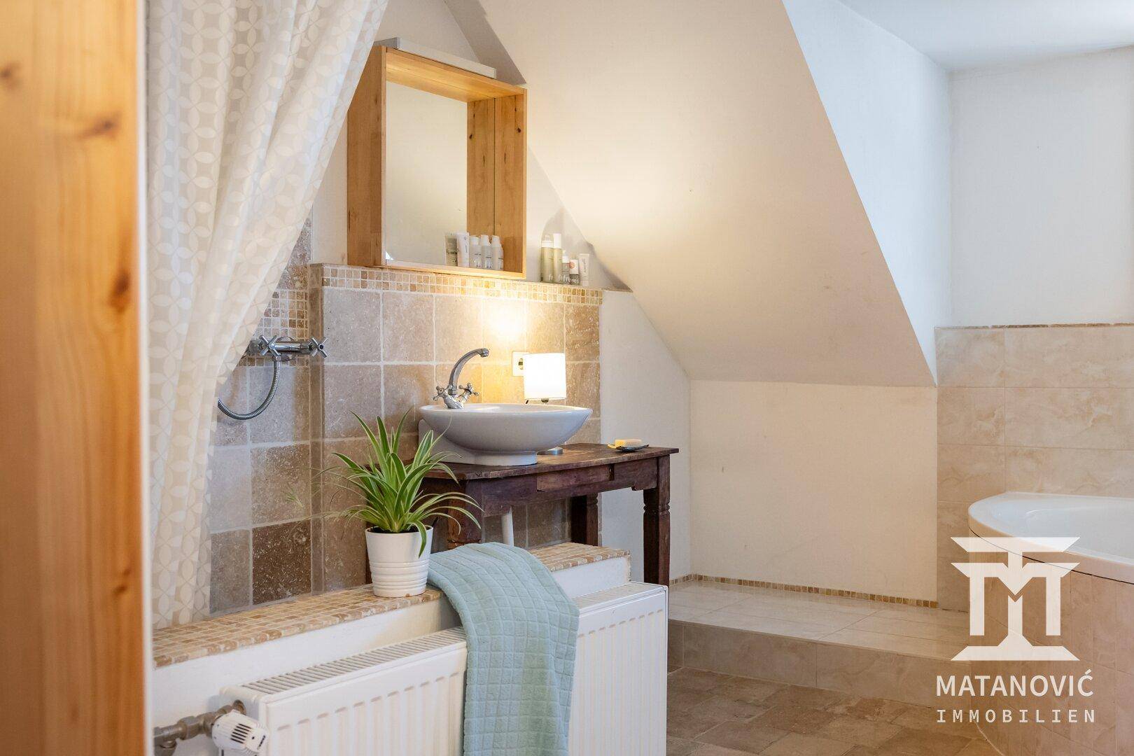 Badezimmer im Dachgeschoss mit Waschbecken auf Holzkonsole, gefliesten Wänden und Badewanne.