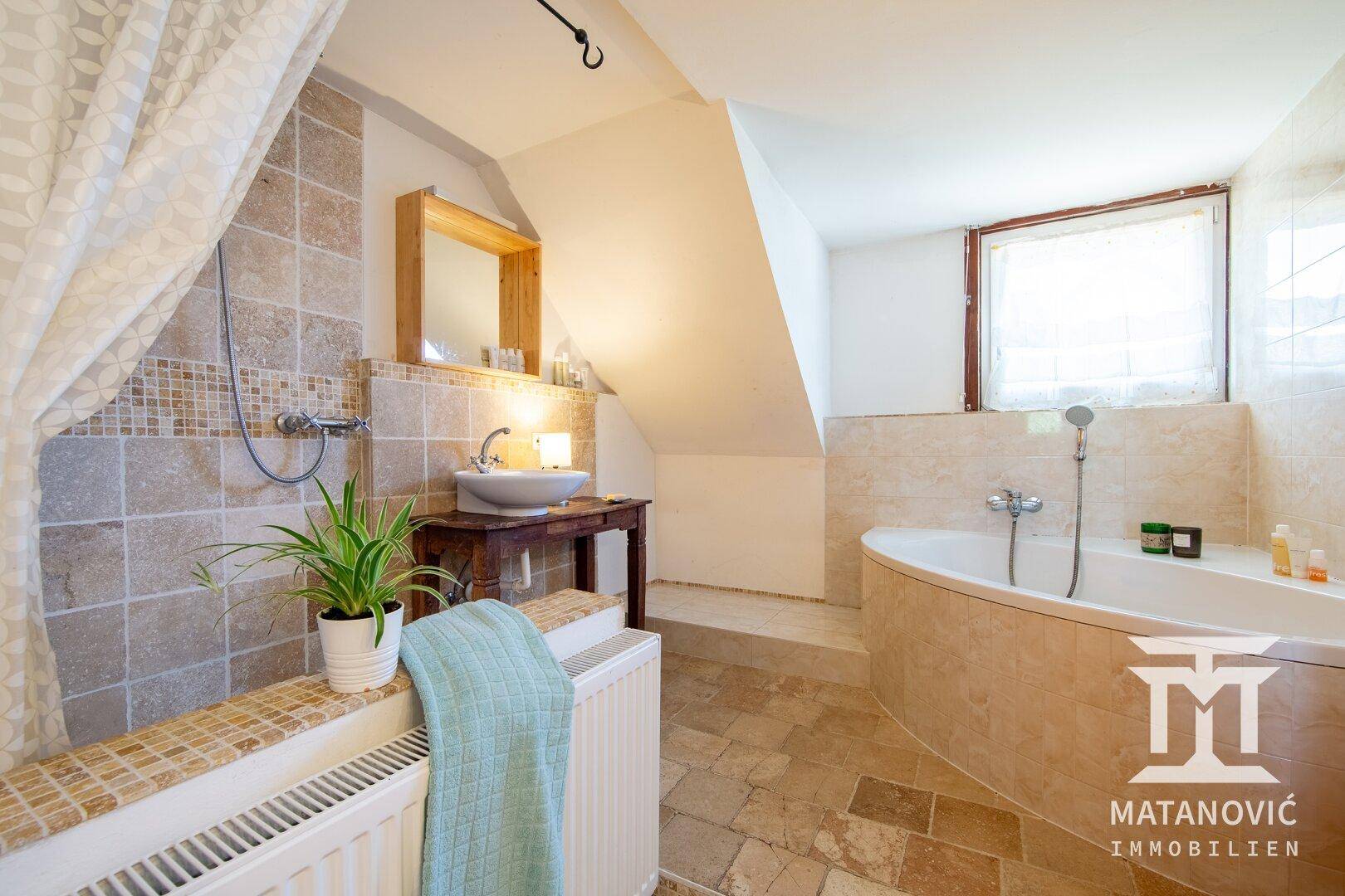 Geräumiges Badezimmer mit Dusche, Waschbecken, Eckbadewanne und Fenster im Dachgeschoss.