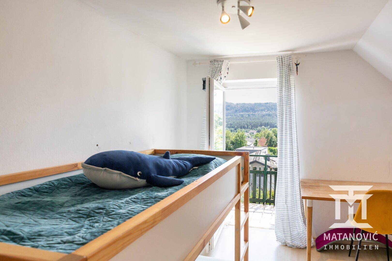 Kinderzimmer mit Etagenbett, Schreibtisch und Balkonzugang mit Blick ins Grüne.