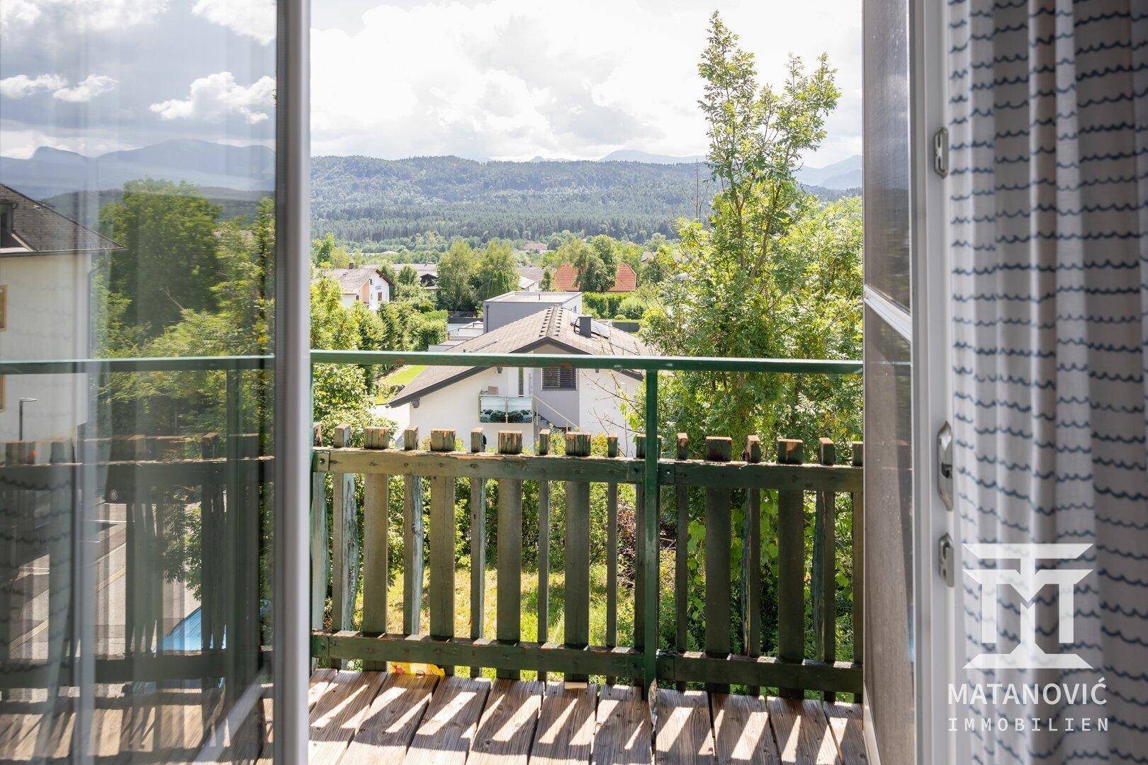Balkon mit Holzboden und Geländer, bietet einen weiten Blick auf die umliegende Landschaft und Berge.