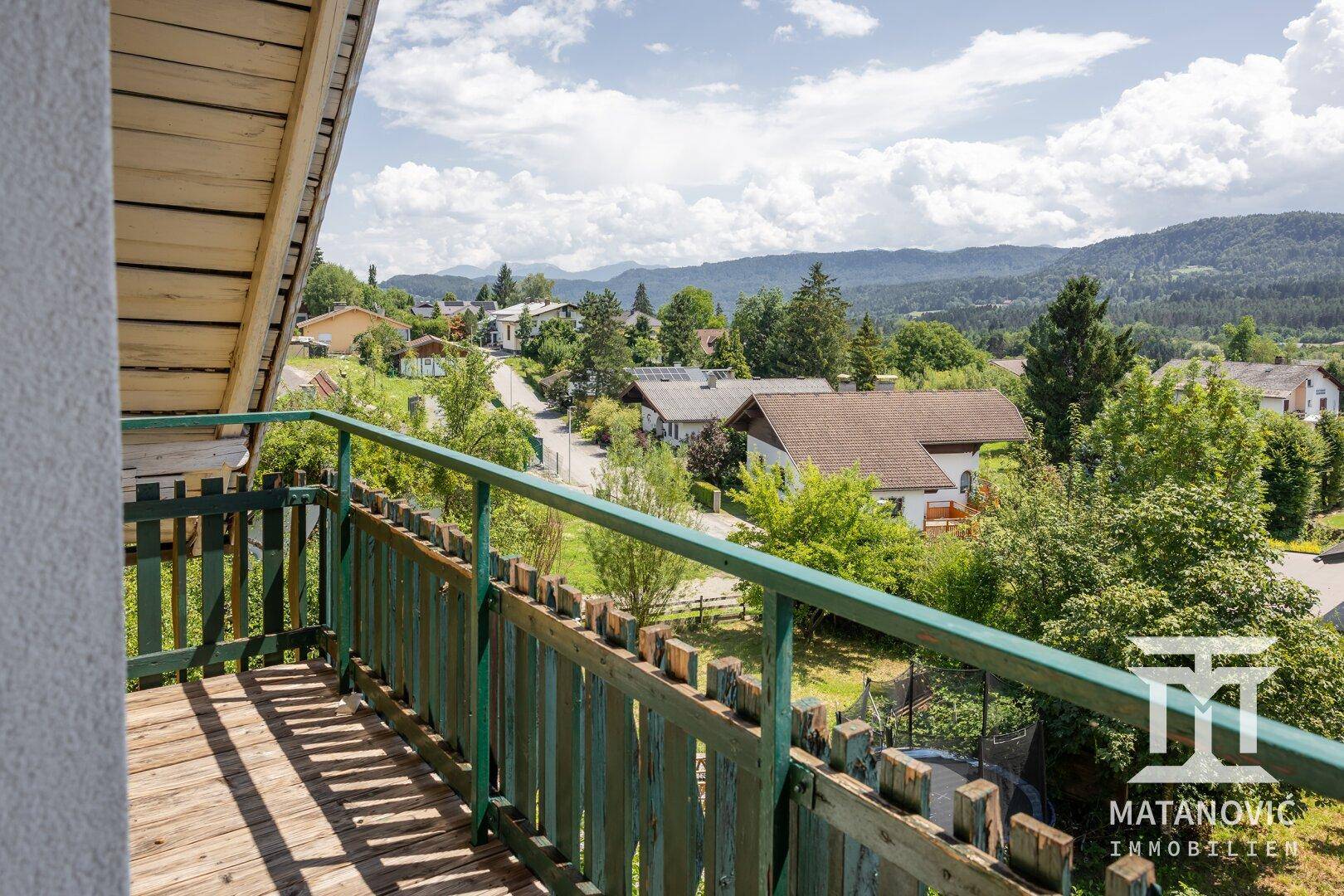 Panoramablick vom Balkon über die Dächer der Häuser, grüne Bäume und ferne Berge.