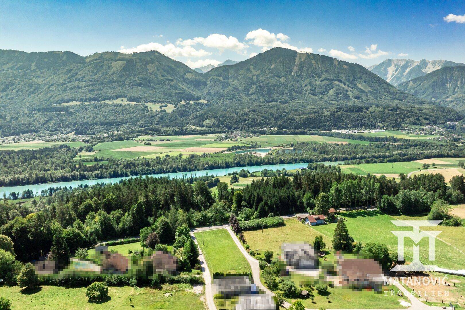 Luftaufnahme einer idyllischen Landschaft mit einem Fluss, dichten Wäldern und majestätischen Bergen.