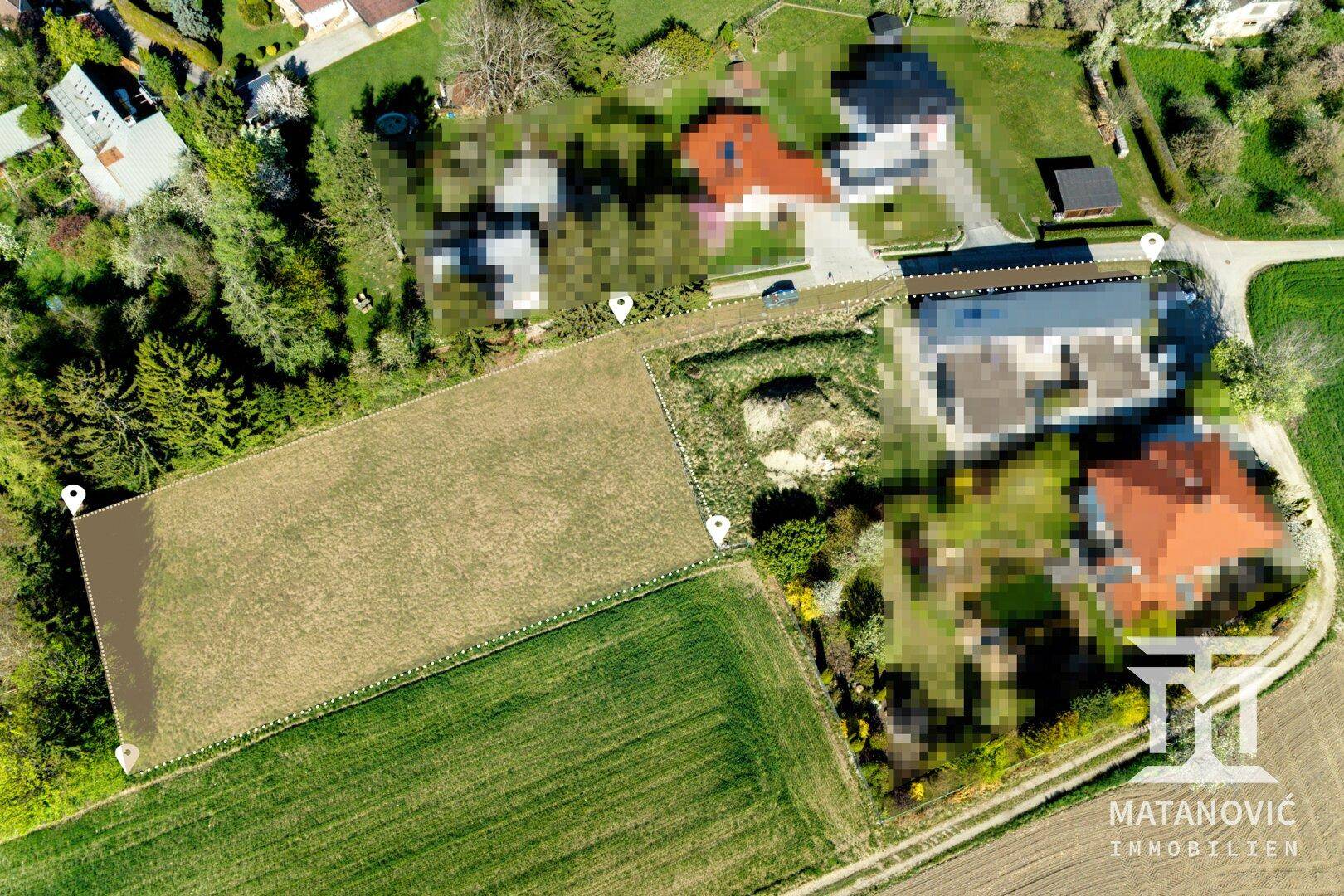 Luftaufnahme einer ländlichen Wohngegend mit Häusern, Feldern und majestätischen Bergen im Hintergrund.