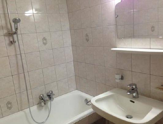 Helles Badezimmer mit Badewanne, Waschbecken und hellen Fliesen, funktional und sauber.