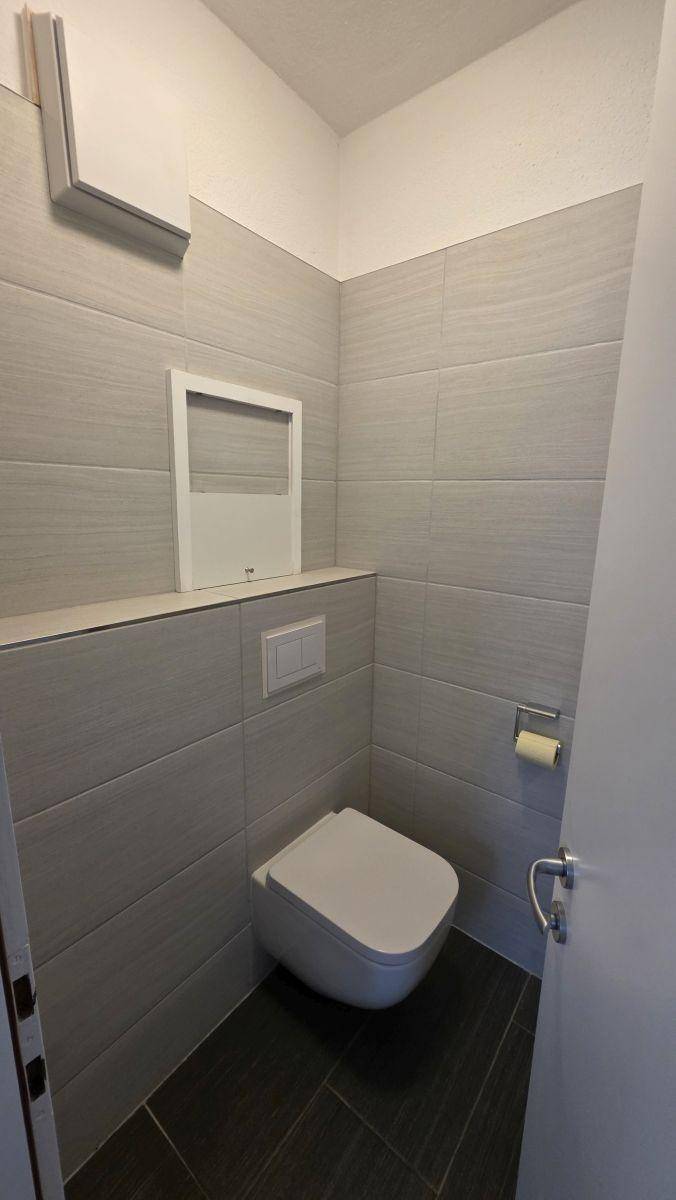 Modern gefliestes Gäste-WC mit wandhängendem WC und Lüftungsanlage.