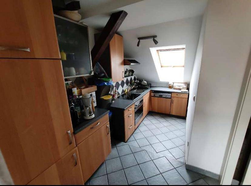 Funktionale Küche mit Holzschränken, Fliesenboden und Dachfenster, unter einer Dachschräge gelegen.