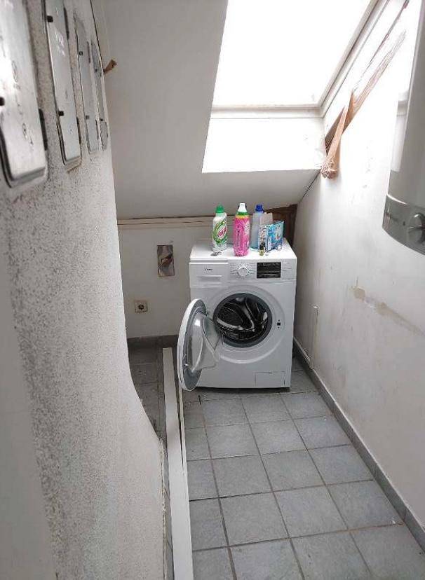 Praktischer Hauswirtschaftsraum mit Waschmaschine, Fliesenboden und Dachfenster unter der Schräge.