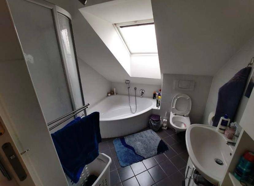 Badezimmer unter der Dachschräge mit Eckbadewanne, Dusche, WC und einem hellen Dachfenster.