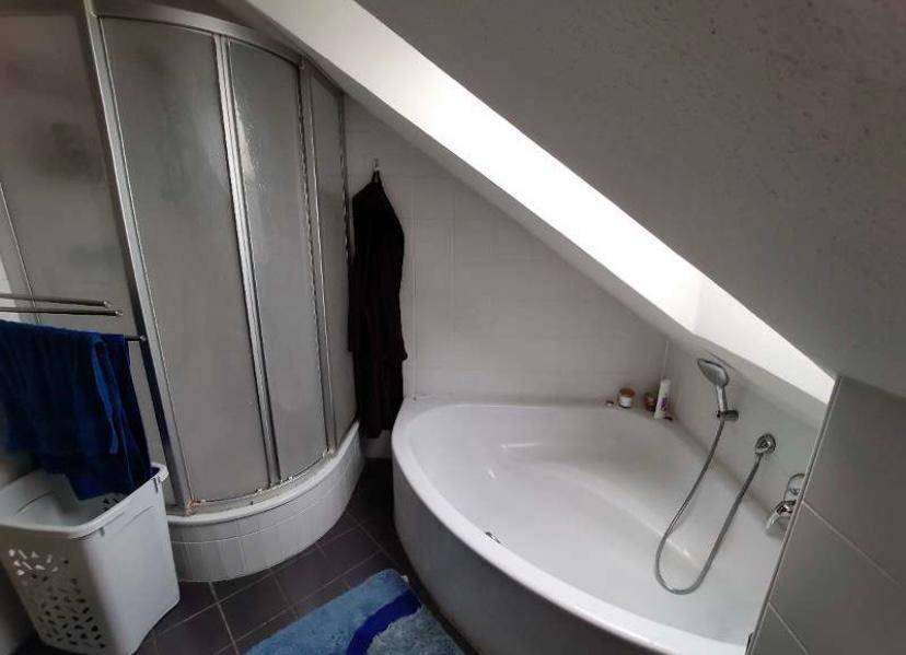 Detailansicht des Badezimmers mit Eckbadewanne und separater Duschkabine unter der Dachschräge.