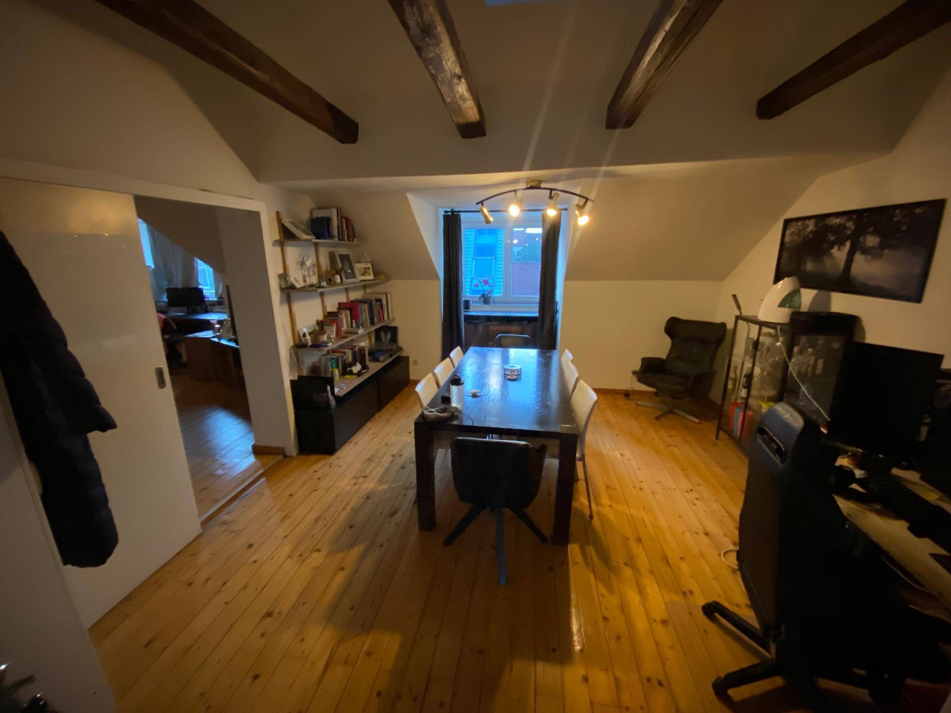 Heller Essbereich mit großem Holztisch, Holzbalken und Dachschrägen, ideal für gemeinsame Mahlzeiten.