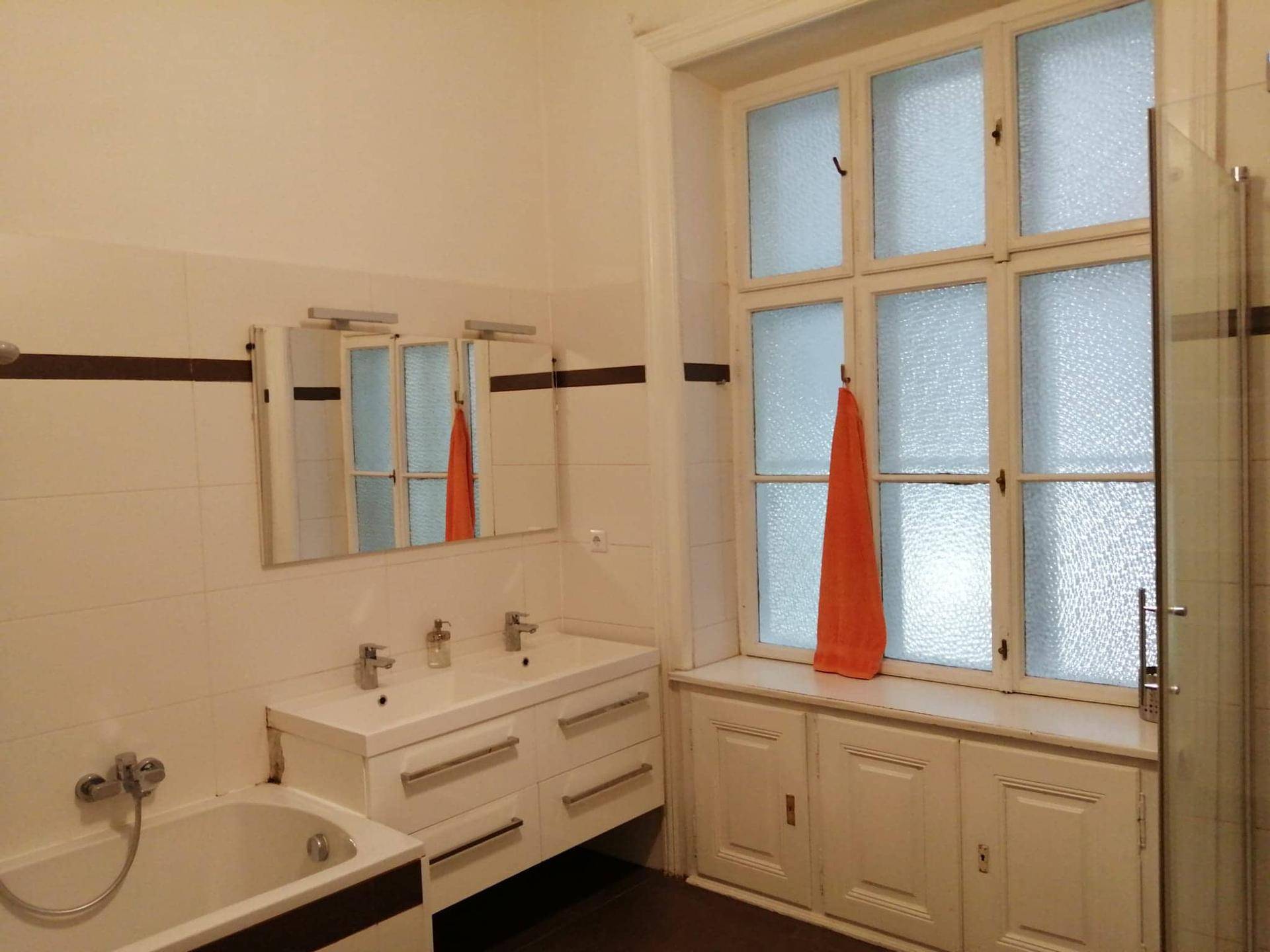 Helles Badezimmer mit Doppelwaschbecken, Badewanne und großem Fenster mit Milchglas für Privatsphäre.