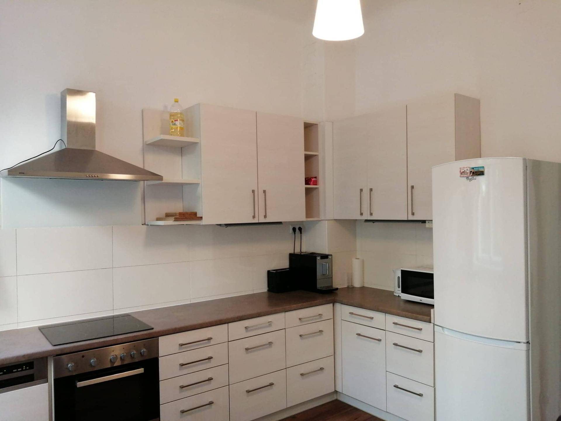 Funktionale Küche mit weißen Schränken, Induktionskochfeld, Backofen und Edelstahl-Dunstabzugshaube.